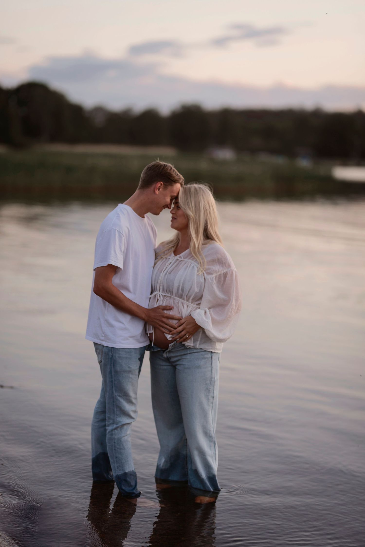 An intimate moment between a couple standing in shallow water at dusk.