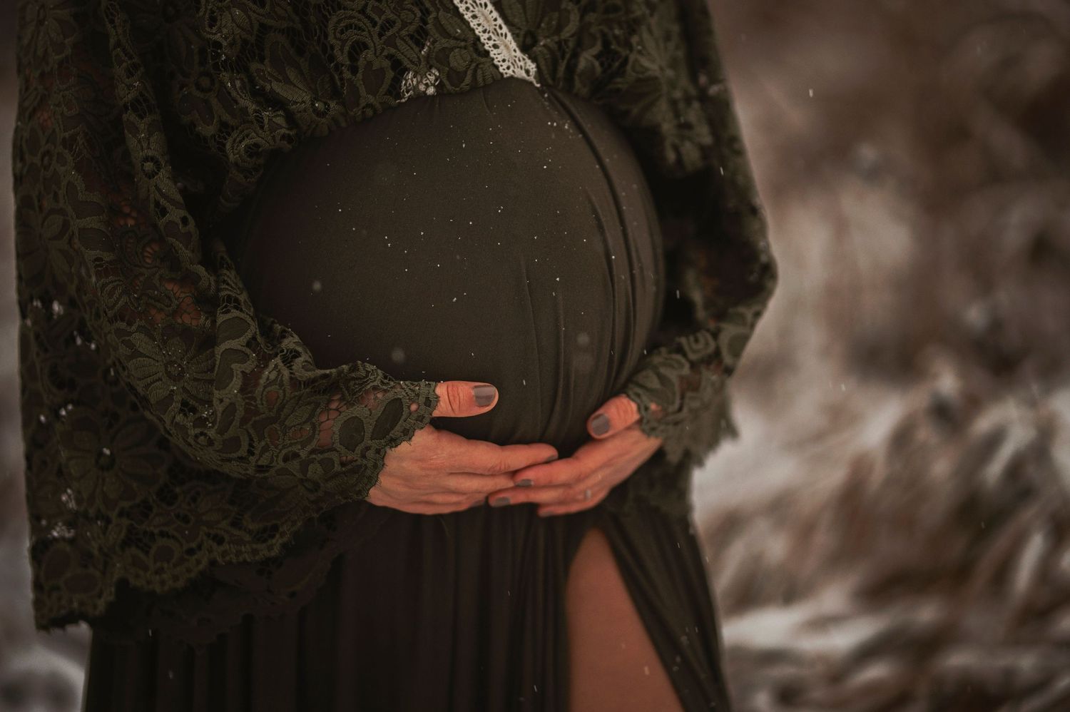 Close-up shot of pregnant belly being cradled by hands in dark winter setting.