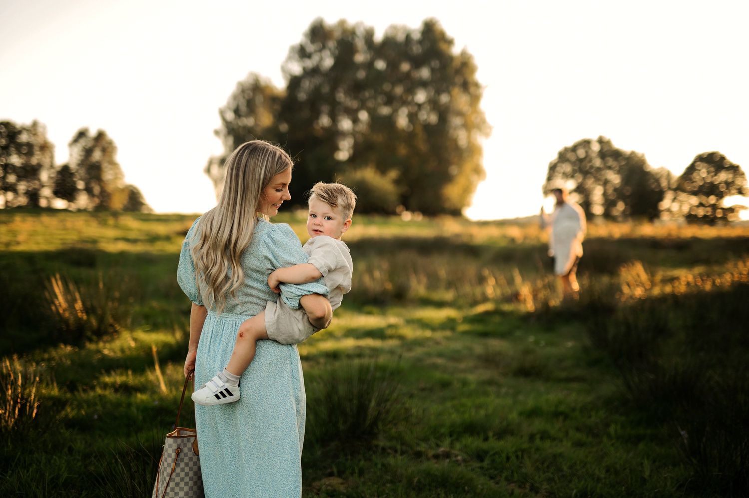 A sunset photoshoot in a grassy field with a person in blue dress holding a young child.