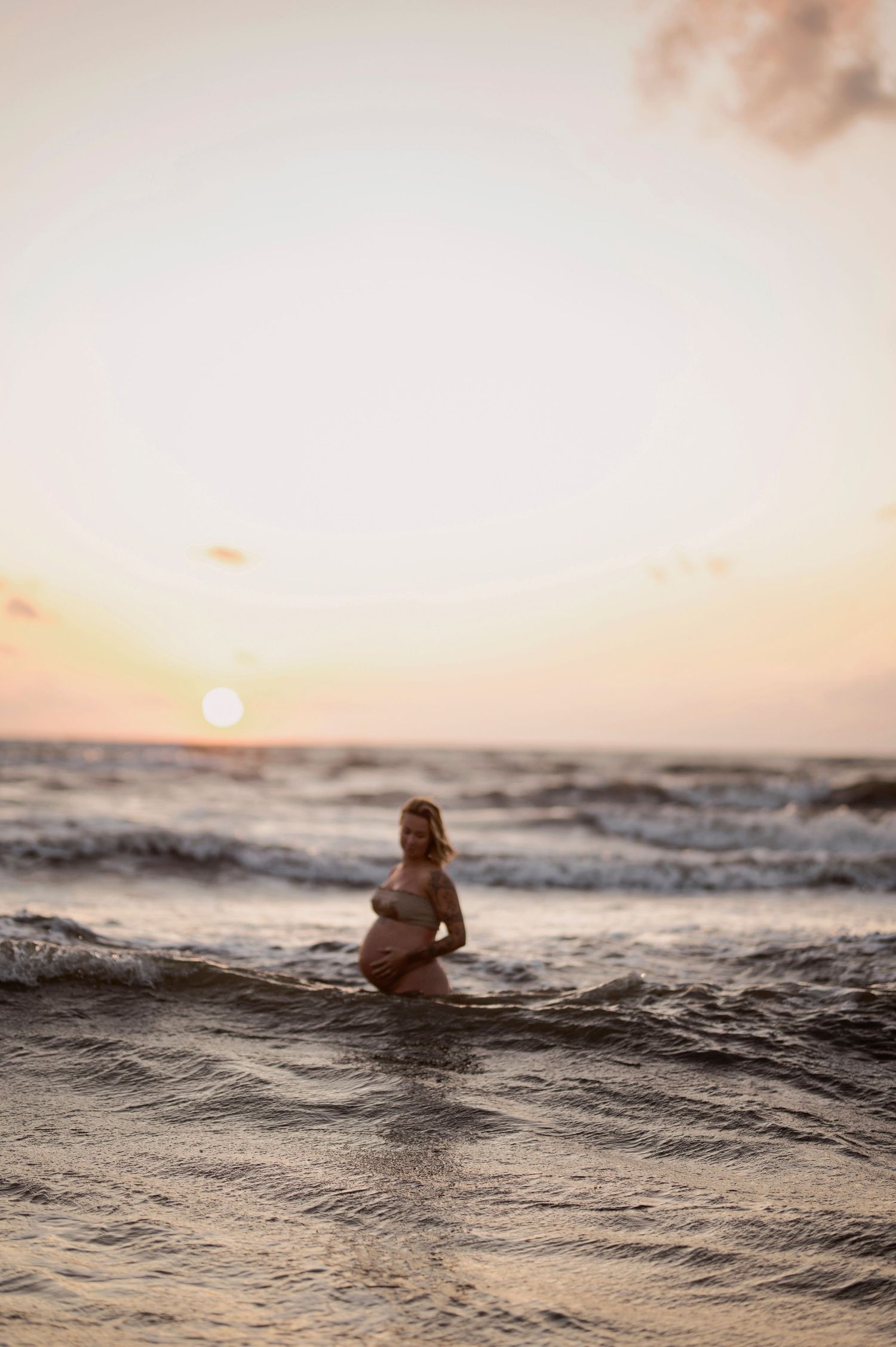 A person sits in ocean waves watching a vibrant sunset over the horizon.