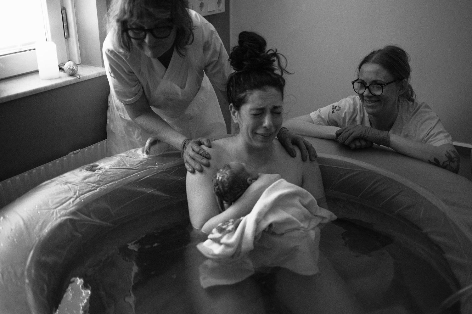 A mother holds her newborn in a birth pool assisted by midwives during a water birth.