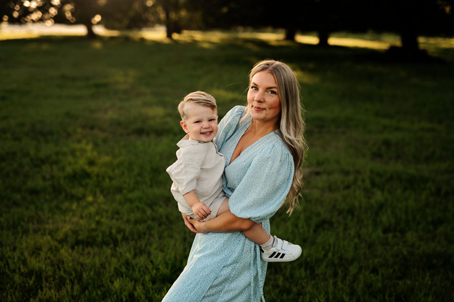 Mother and child portrait in blue dress against sunset lit park setting.