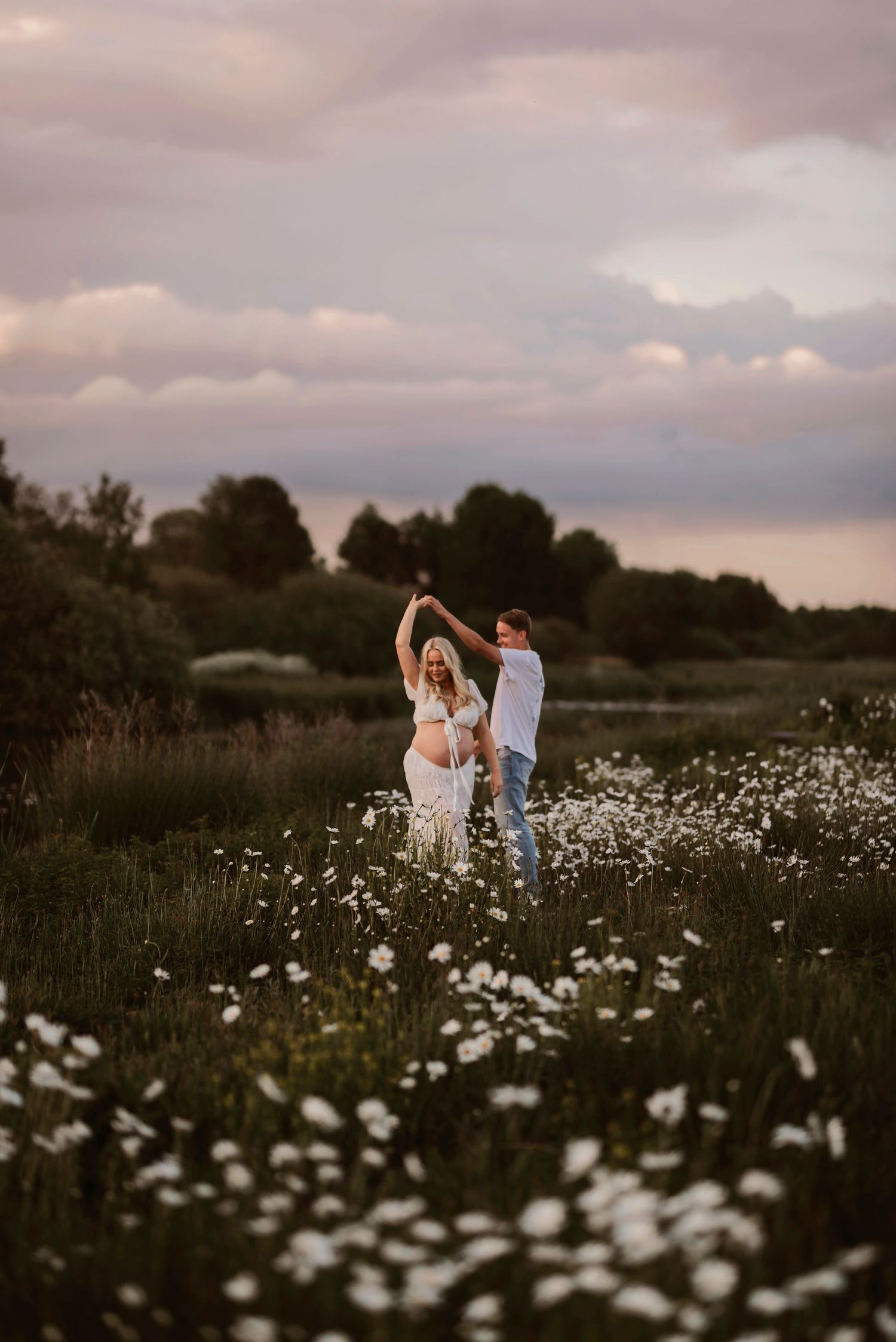 Romantiskt par dansar i blomsteräng vid solnedgången i Skåne nära Hässleholm – med dramatiska moln som bakgrund.