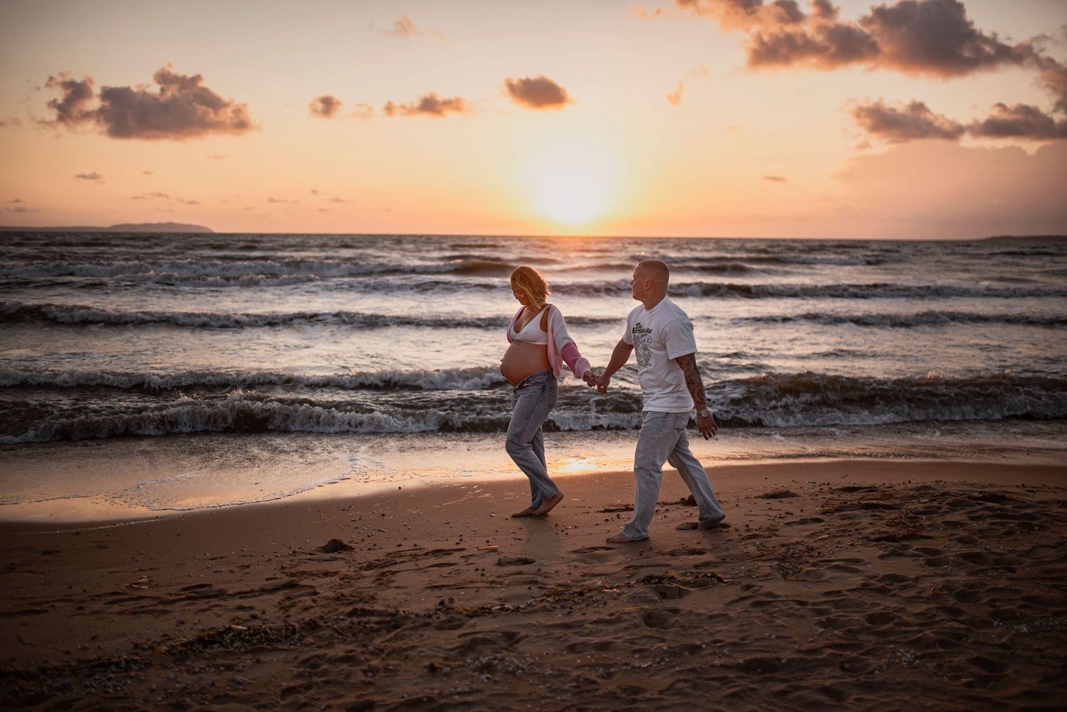 A couple walks hand in hand on a beautiful beach at sunset with waves crashing in the background.