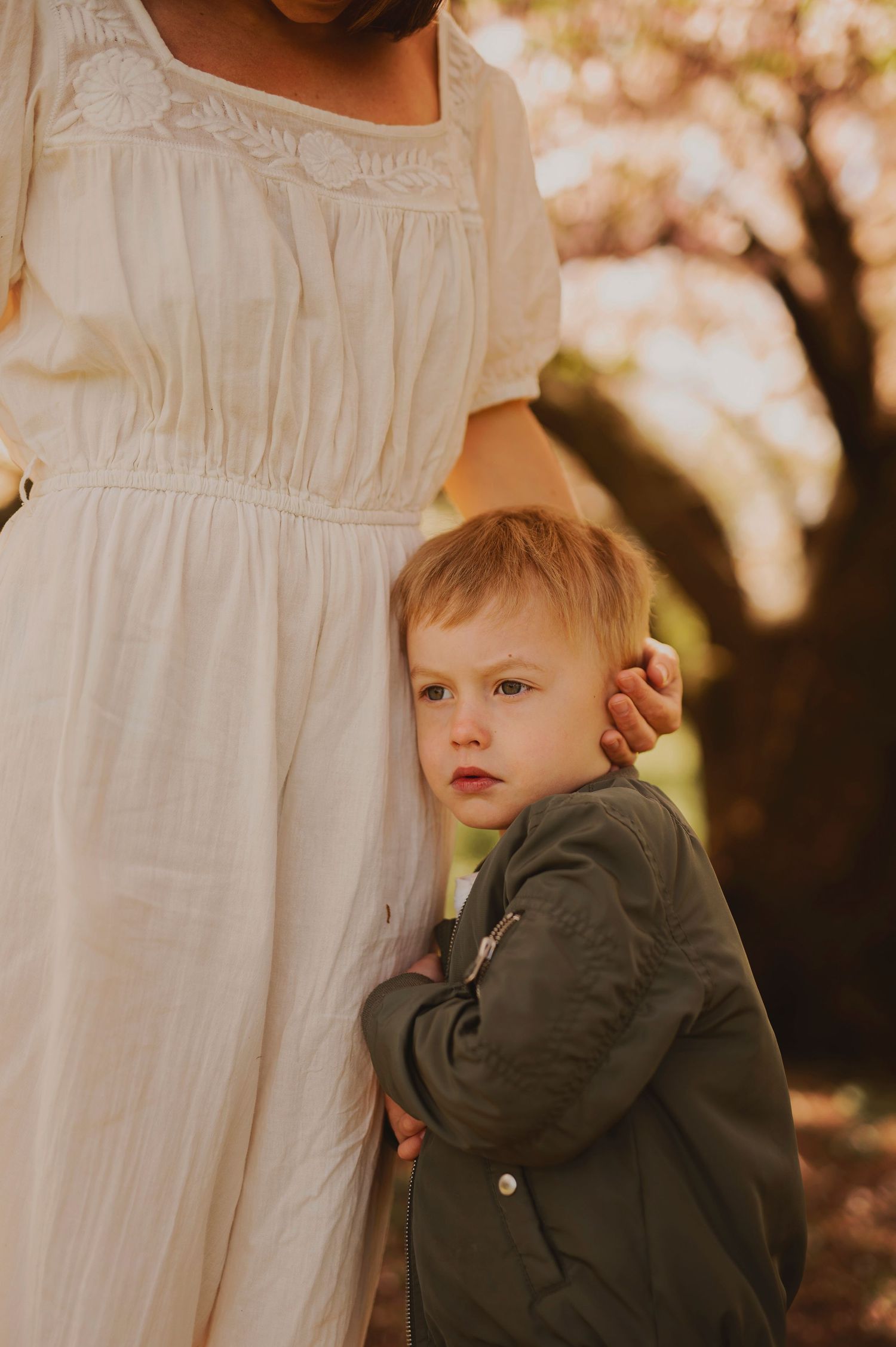 Tender moment captured under cherry blossoms in vintage-style white dress.