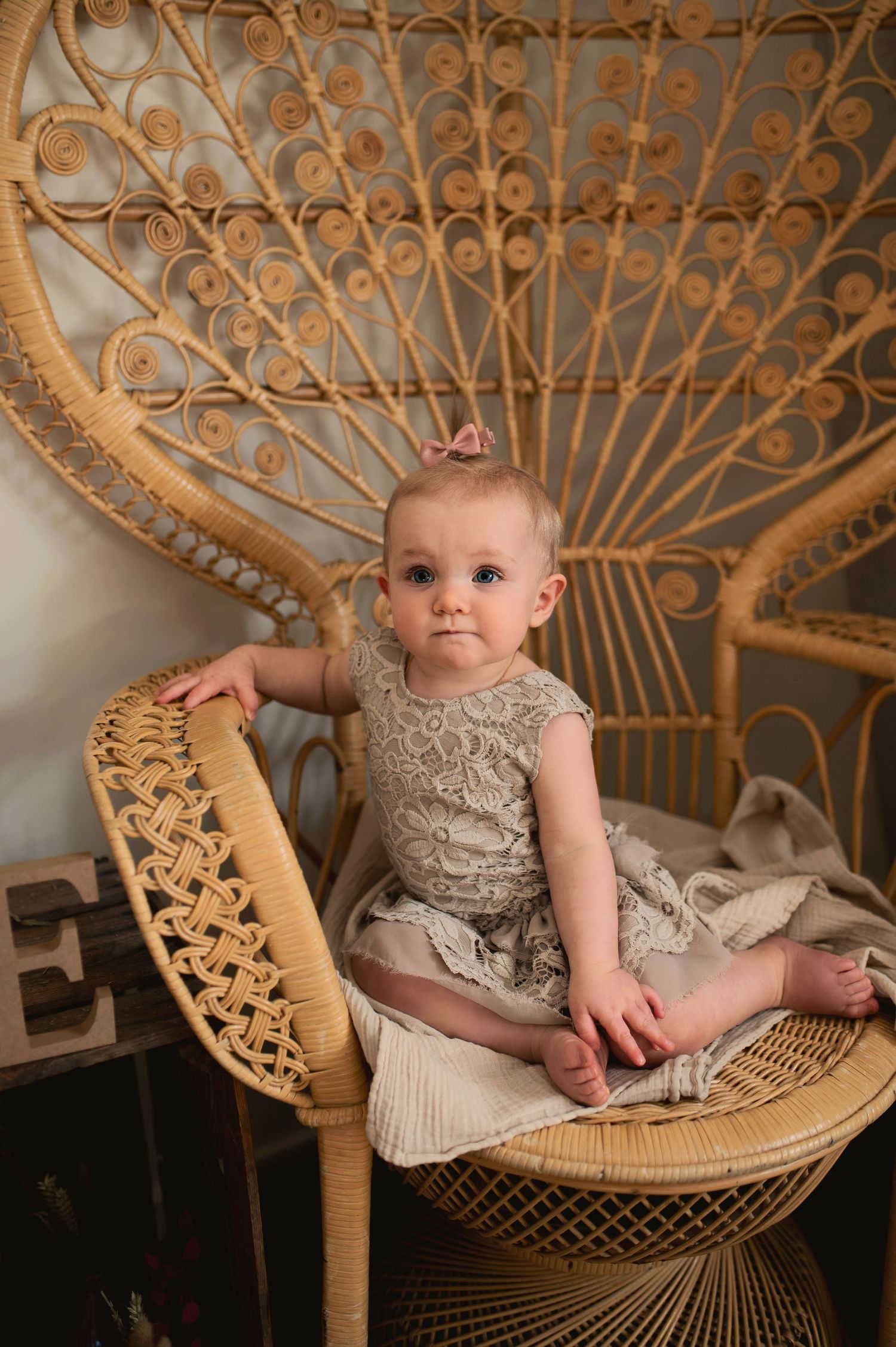 A vintage-style portrait of a baby seated in a large woven peacock chair.