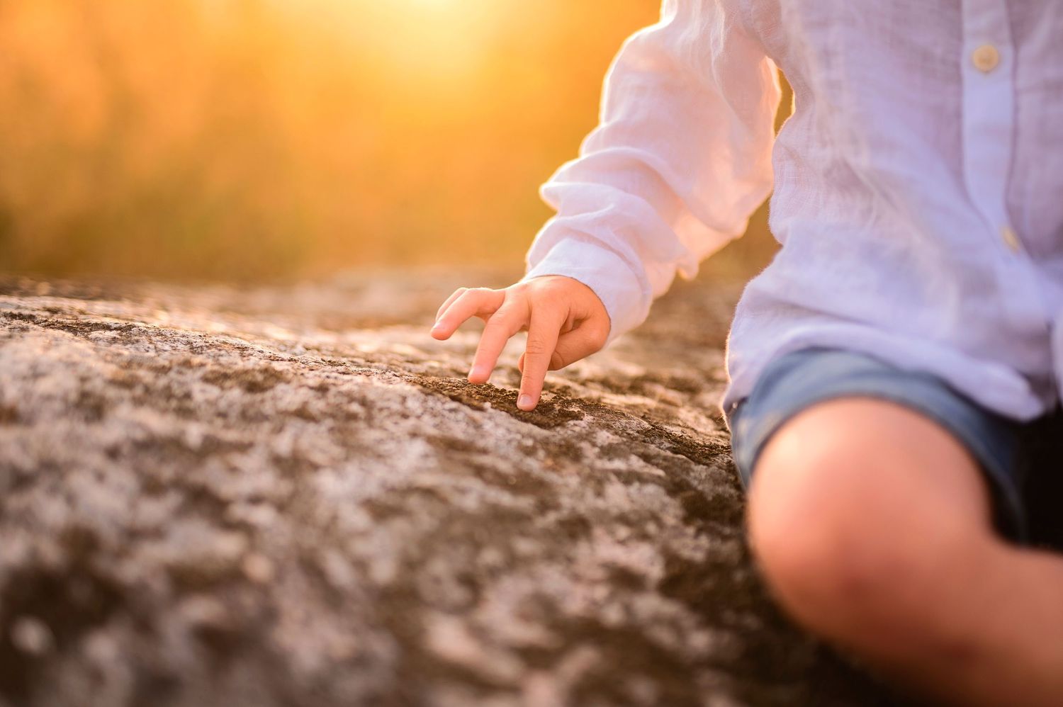 Close-up of a hand touching rough stone surface during golden sunset.