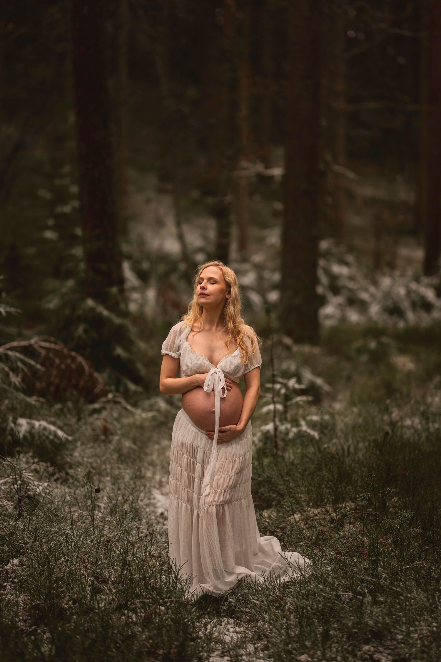 Vacker gravid kvinna på fotografering i en skog med mossa. Fotograf är Lovestories By Sara.