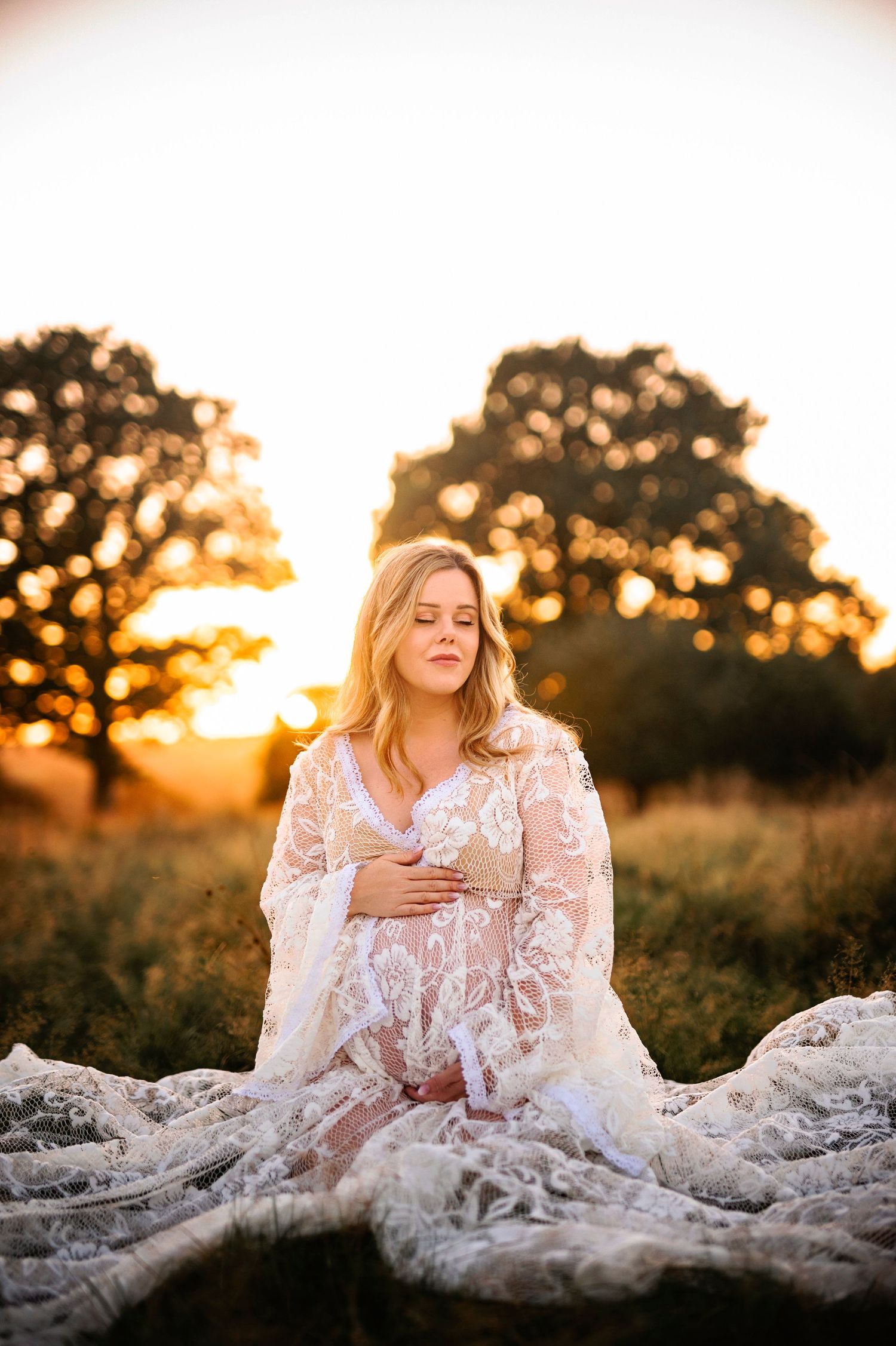 Intimate maternity moment captured in white lace dress during sunset golden hour.