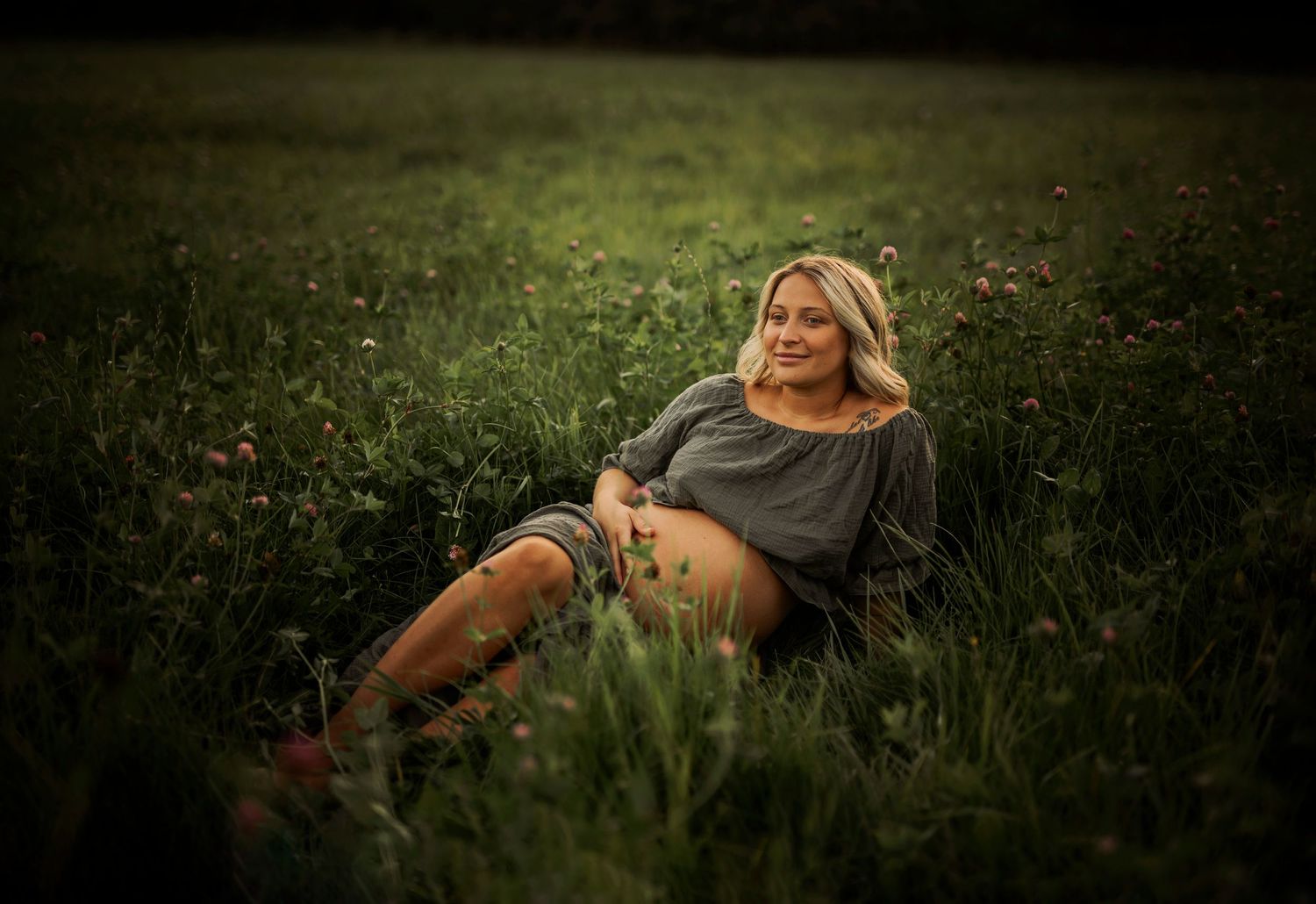 Serene maternity photo in field featuring gray dress and brown boots at dusk.