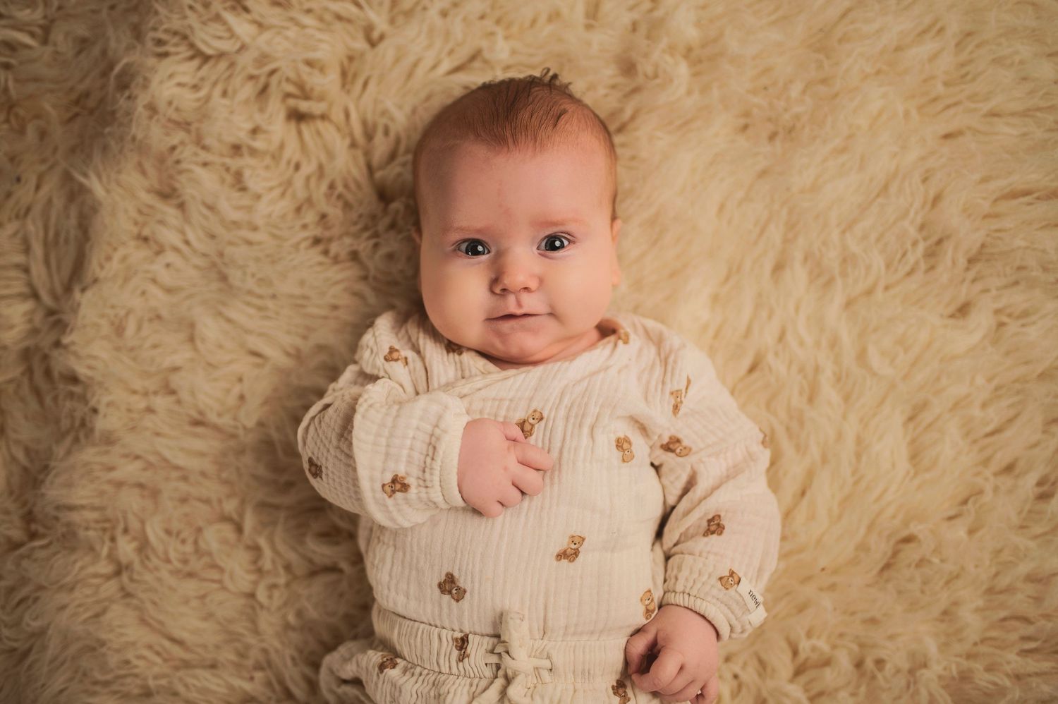 Baby in cream knit sweater with embroidered details on plush fur rug.