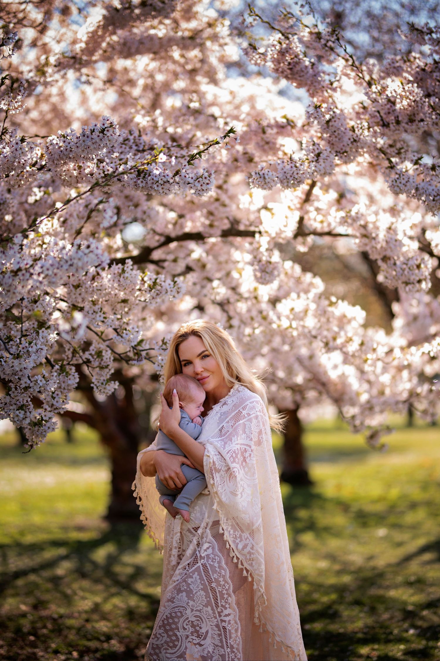 Tender motherhood moment captured under blooming cherry trees.