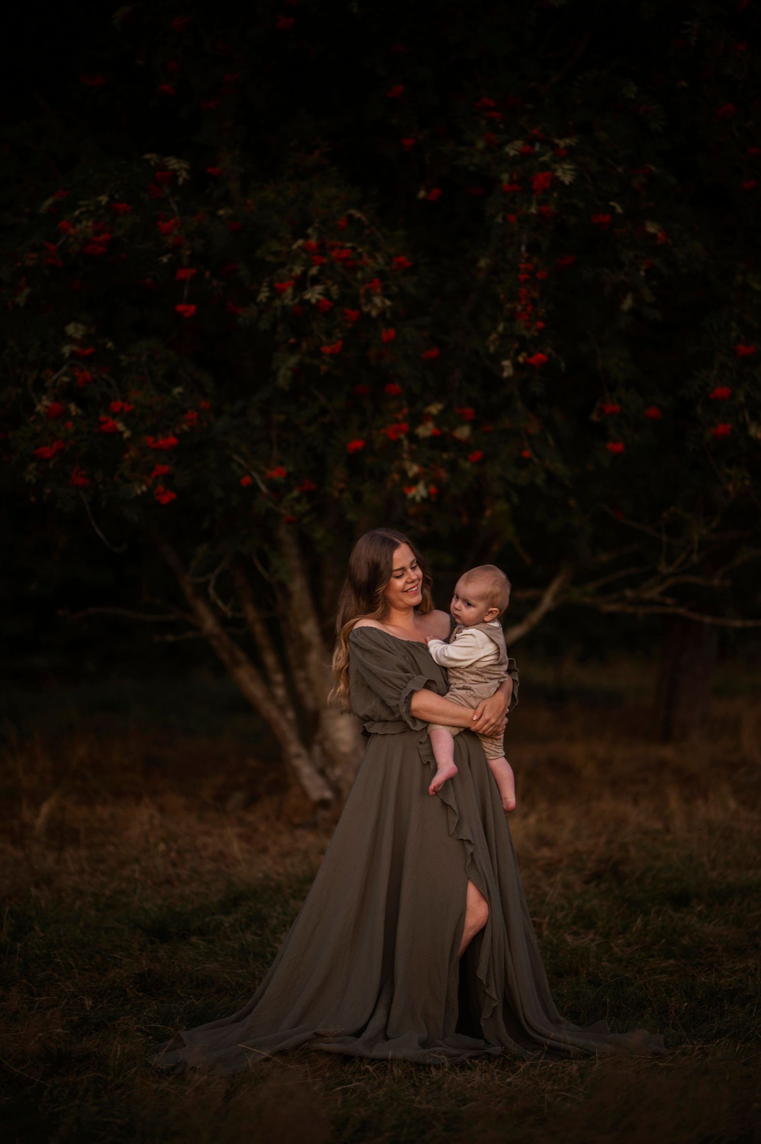 A flowing grey dress creates drama against red berry trees at dusk.