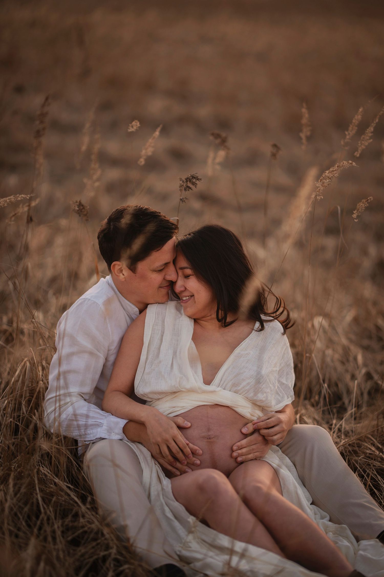 A couple shares an intimate moment in a field of golden wheat during sunset, showing affection and tenderness.