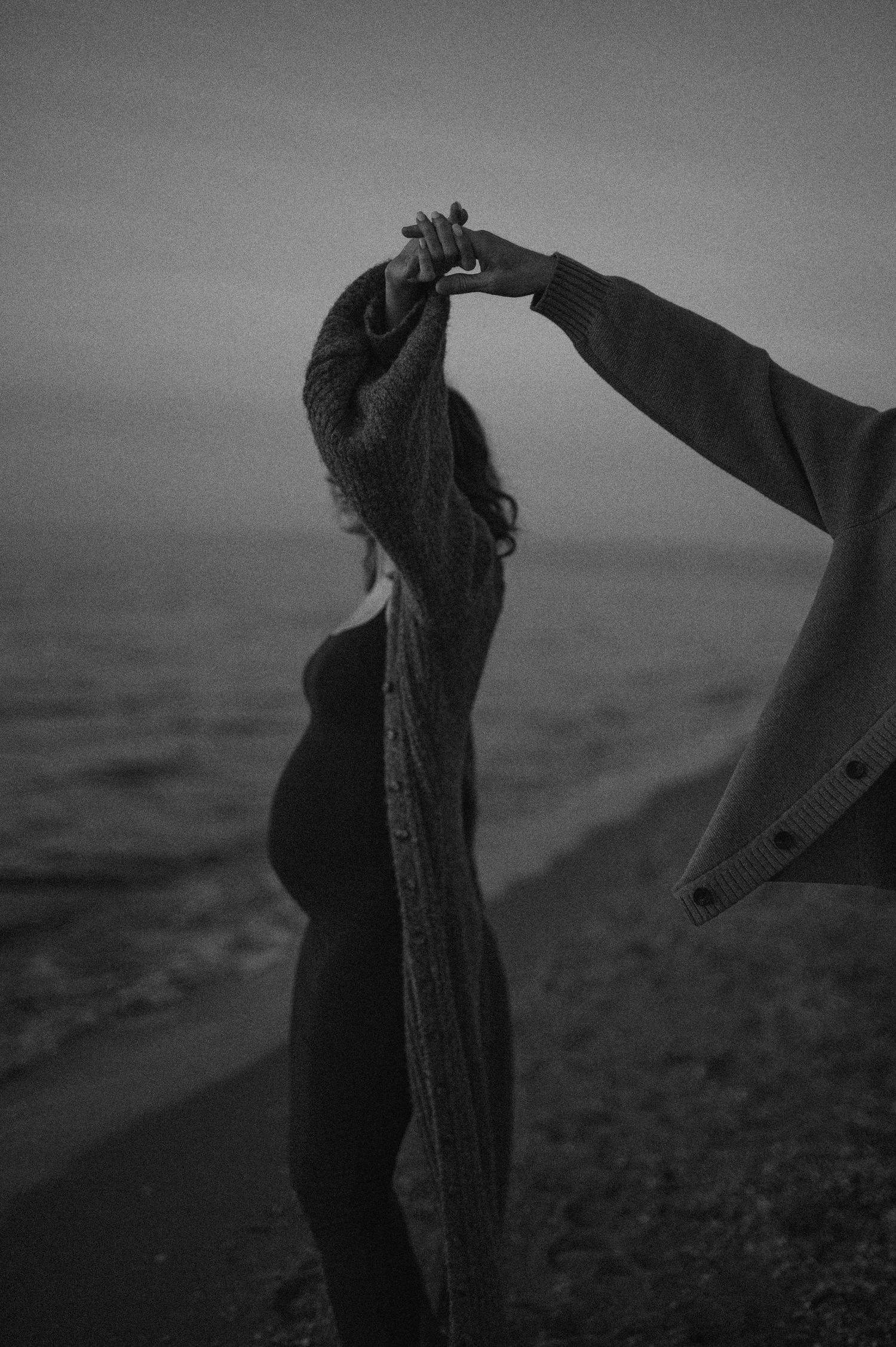 A silhouetted figure stands at the edge of a cliff overlooking the ocean in a moody black and white photograph.