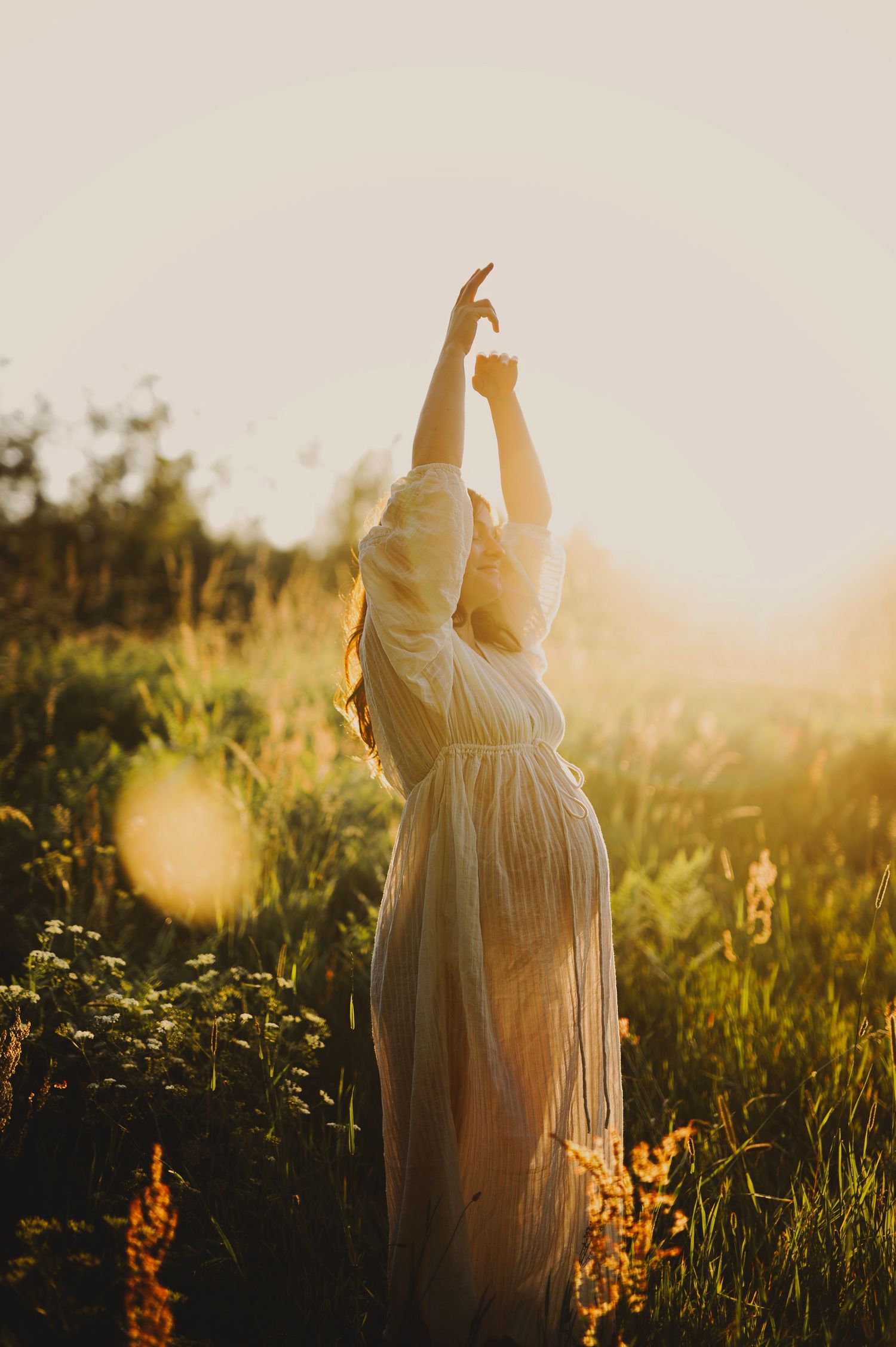 A ethereal maternity photo shows a flowing white dress silhouetted against golden sunset light.