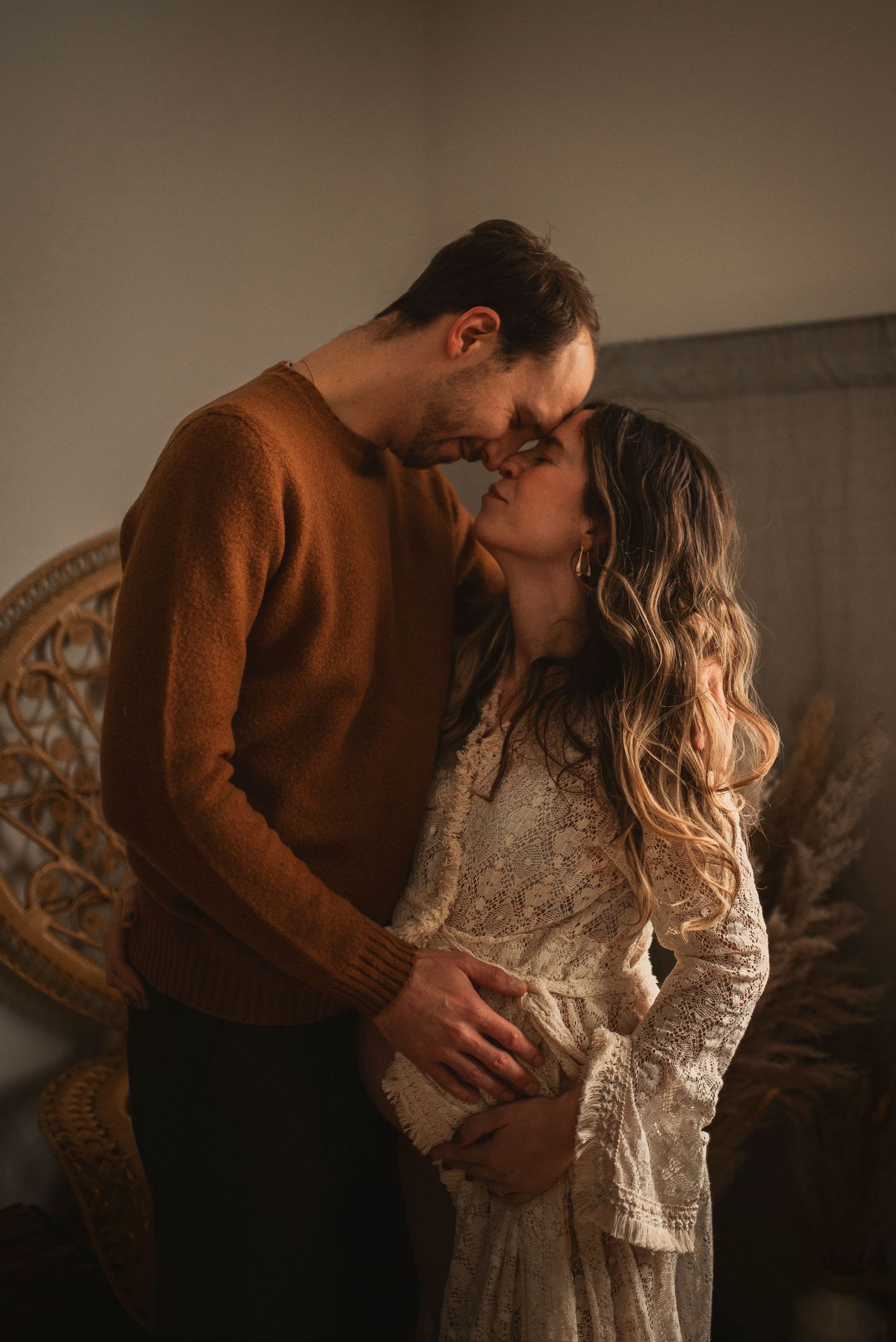 Romantic indoor portrait of a couple in warm earth tones against a textured backdrop.