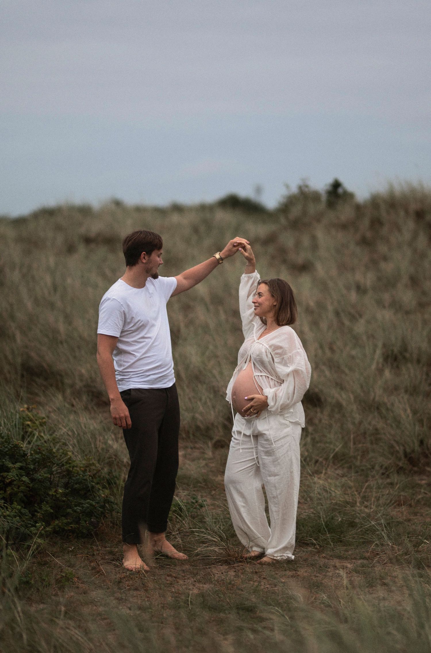 A couple shares a romantic dance moment on a coastal hillside.