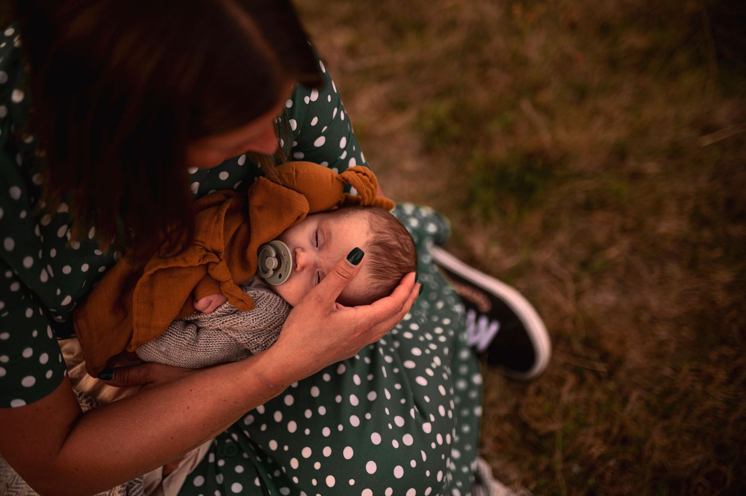 Person wearing polka dot dress holding something while sitting in field at sunset.