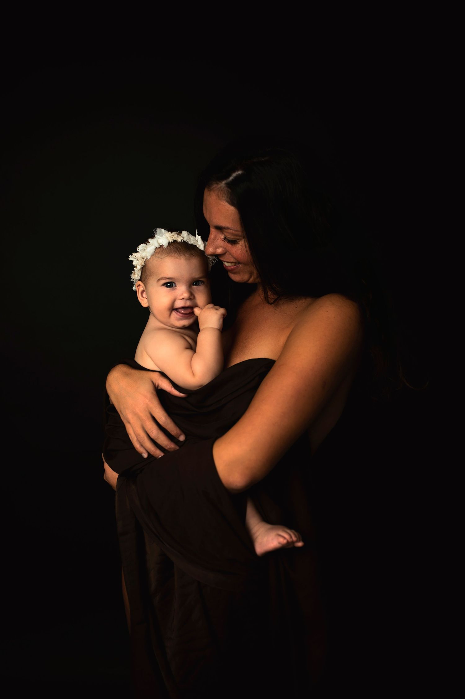 Intimate low-light portrait with baby against dark background.