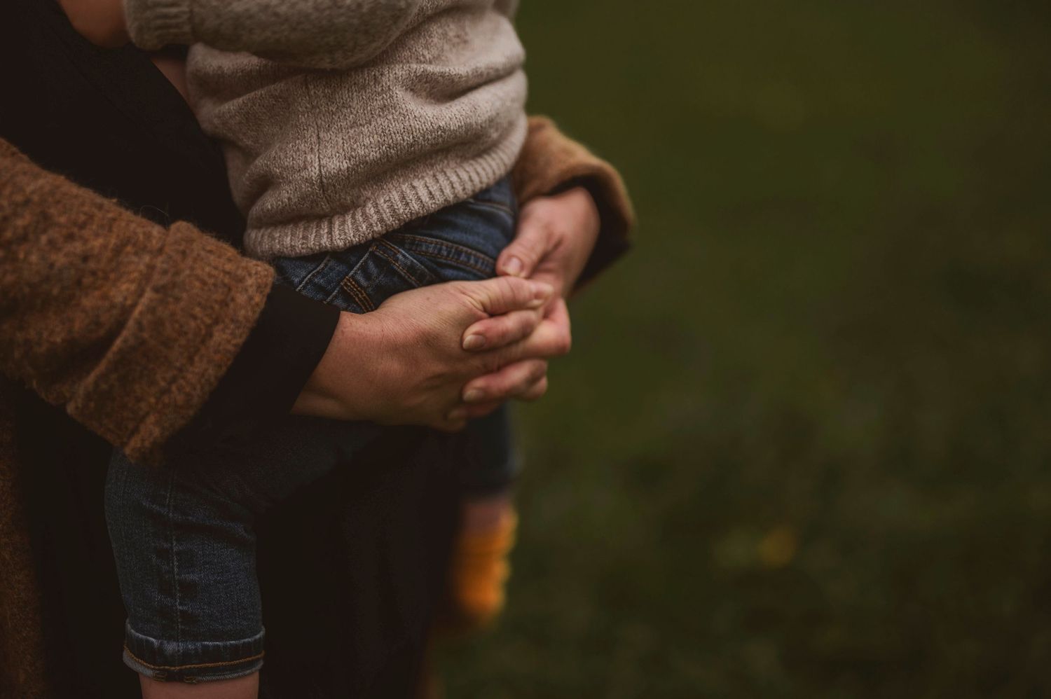 Close-up of hands holding a small child wearing jeans against a dark green background.