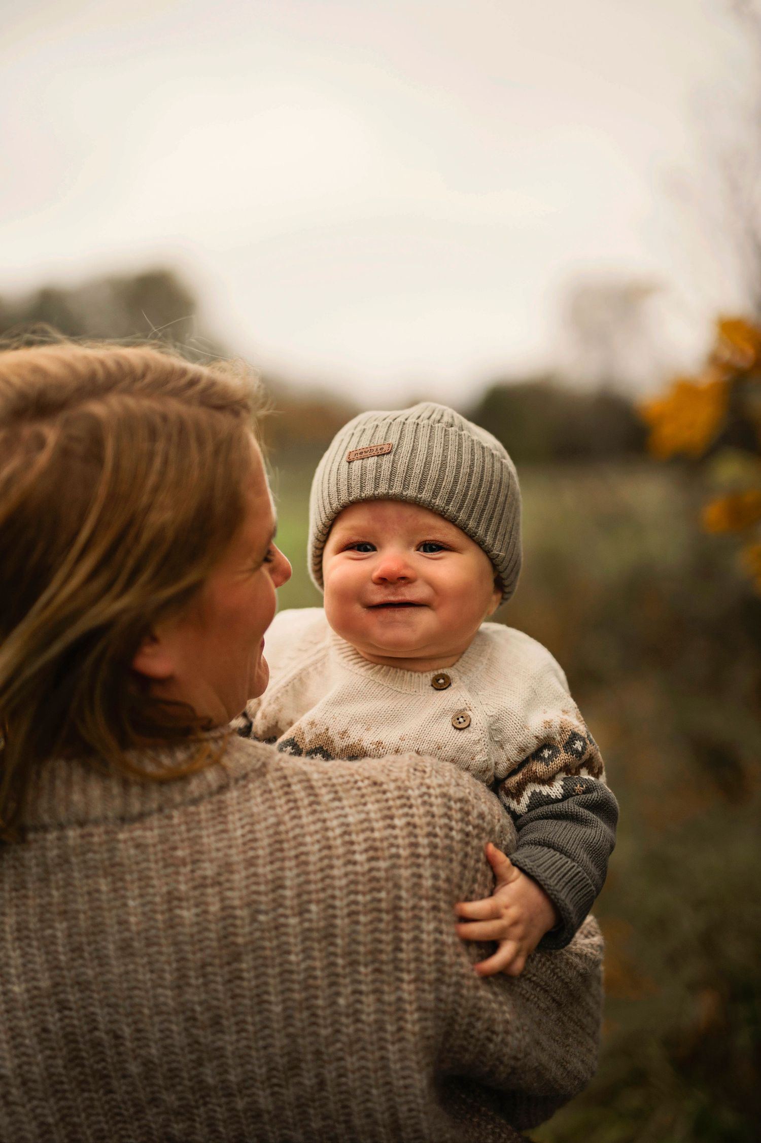 A sweet candid moment between parent and smiling baby in fall weather.