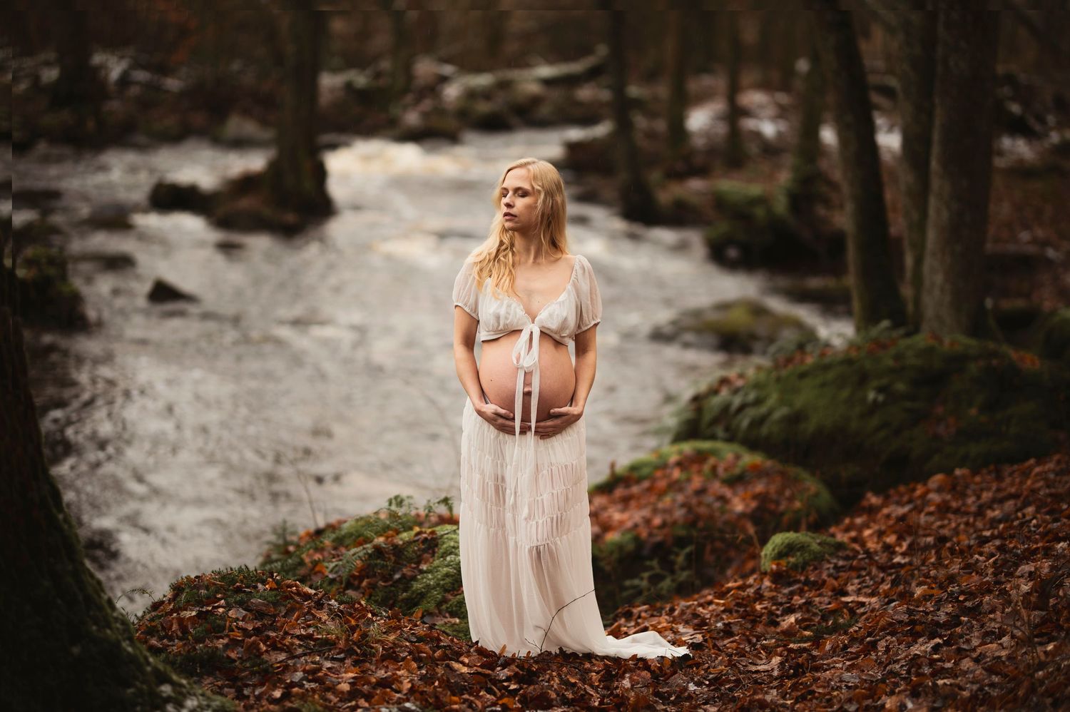 Vacker gravid kvinna på fotografering vid en bäck. Fotograf är Lovestories By Sara.