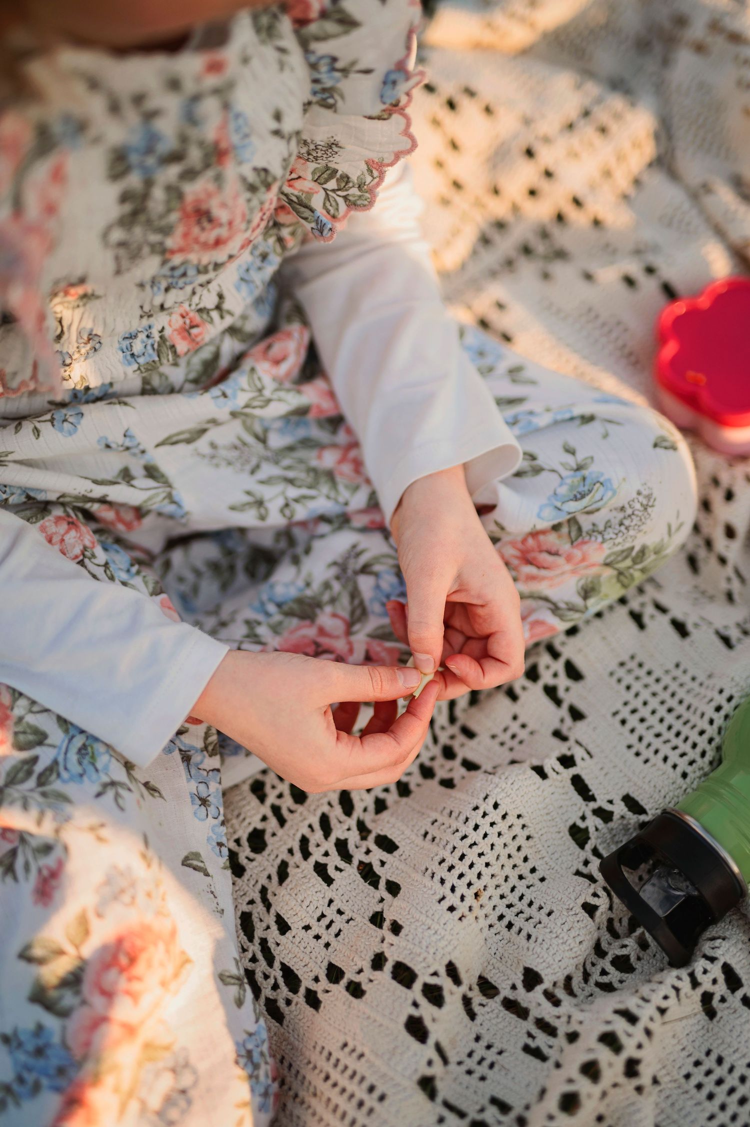 Close-up of hands resting on floral and lace blanket during outdoor picnic.