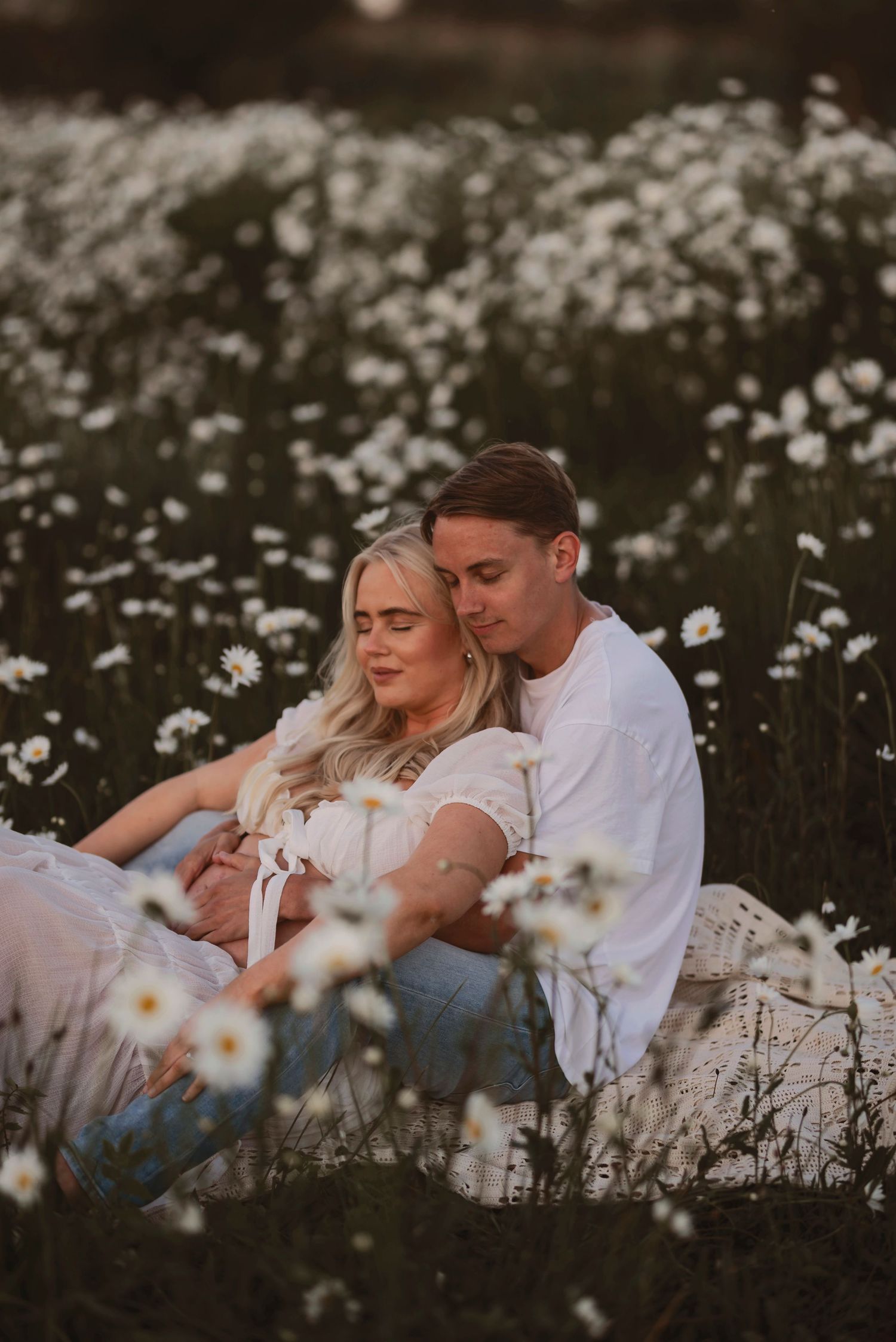 Romantic couple's maternity photos in blooming wildflower meadow with warm sunset glow.