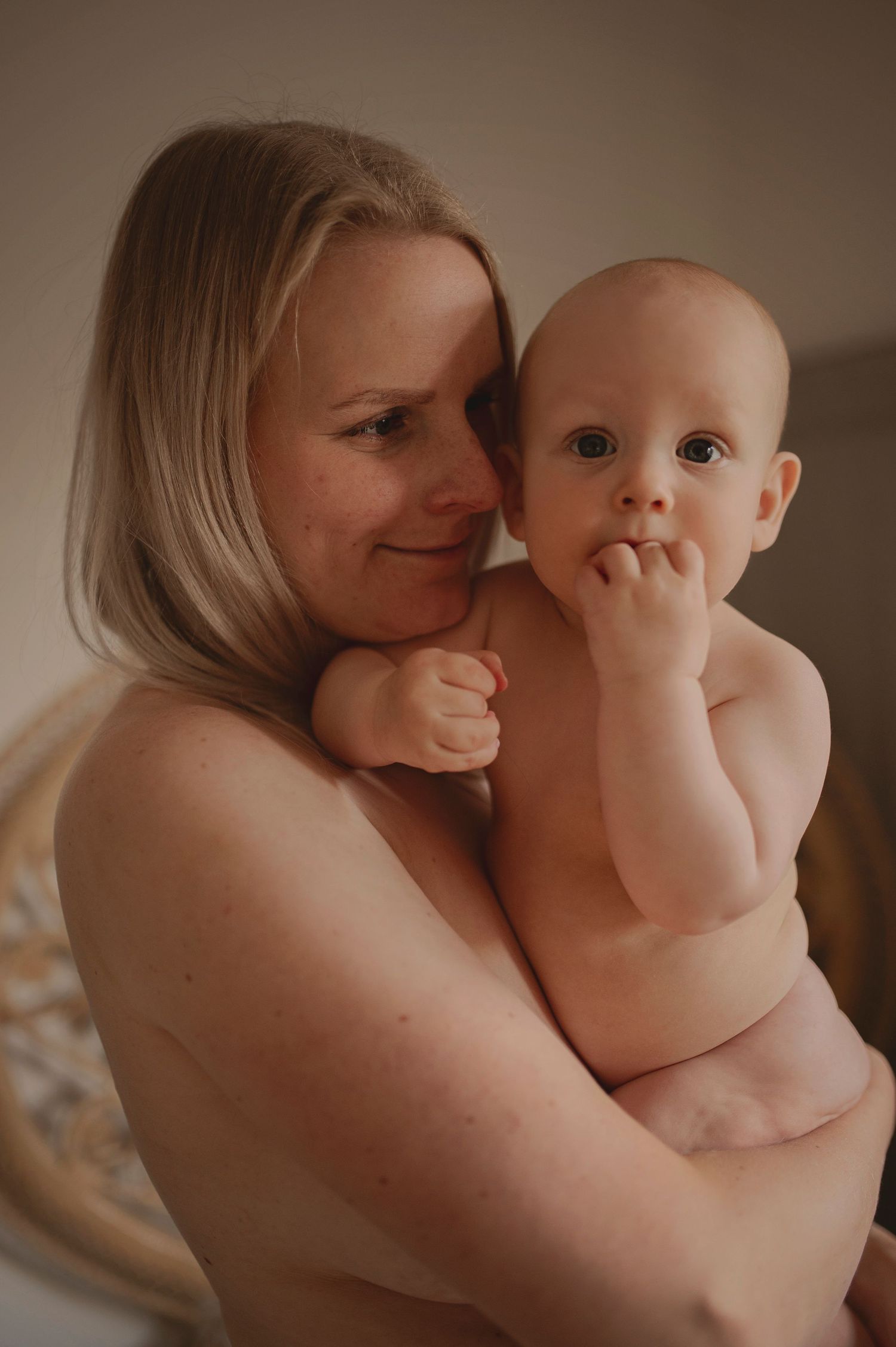 Intimate portrait of mother and infant sharing a tender moment in warm lighting.
