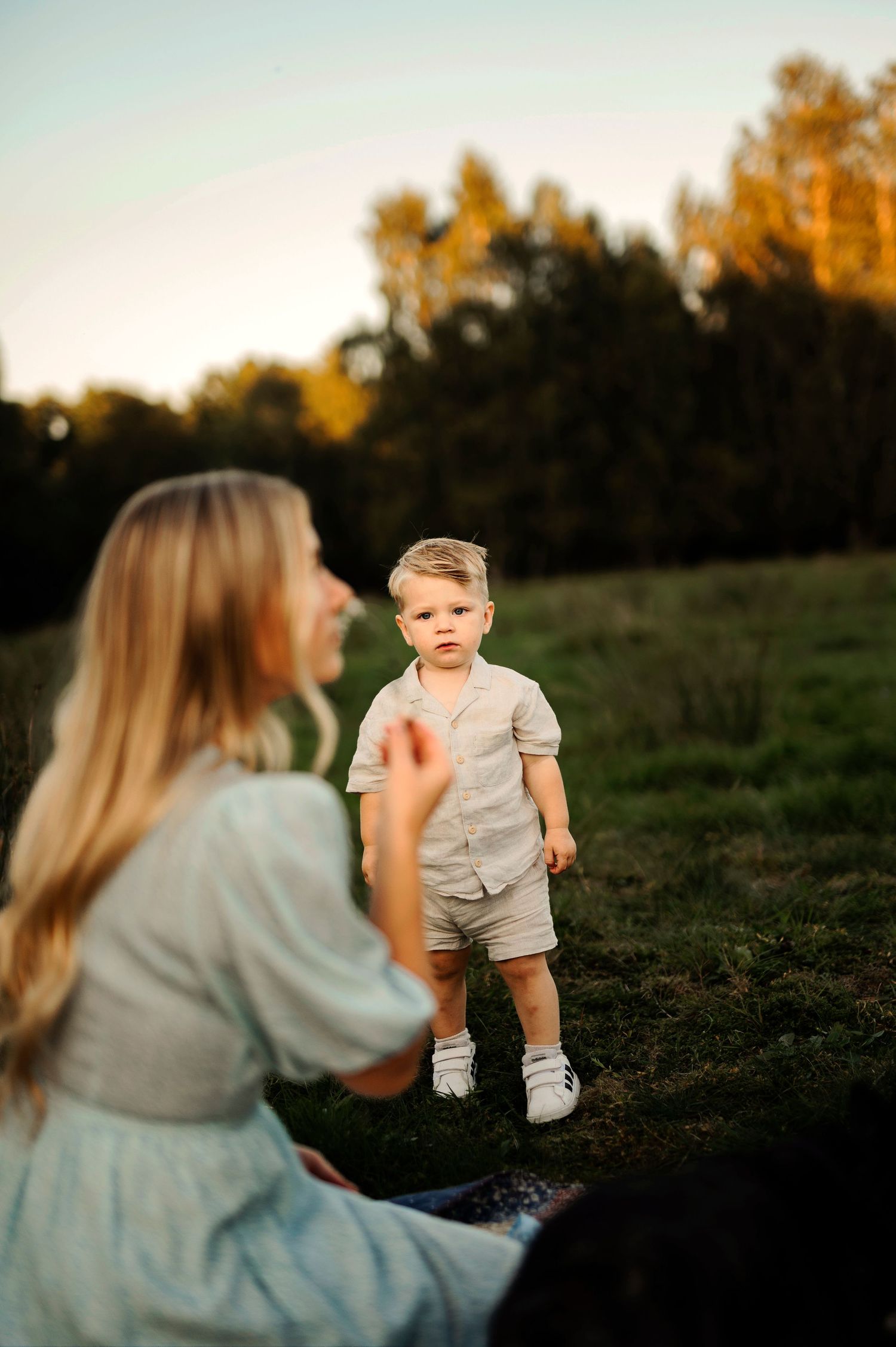 A touching moment at sunset in a grassy field wearing light colored clothing during golden hour.