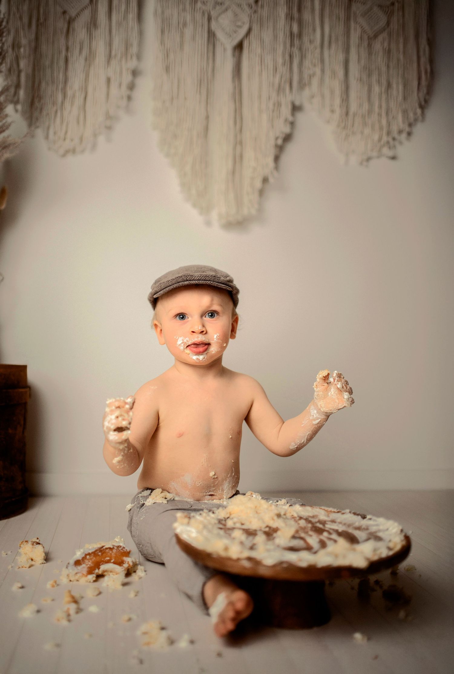 A baby in a flat cap playfully smashes and eats cake in a messy progression of photos.
