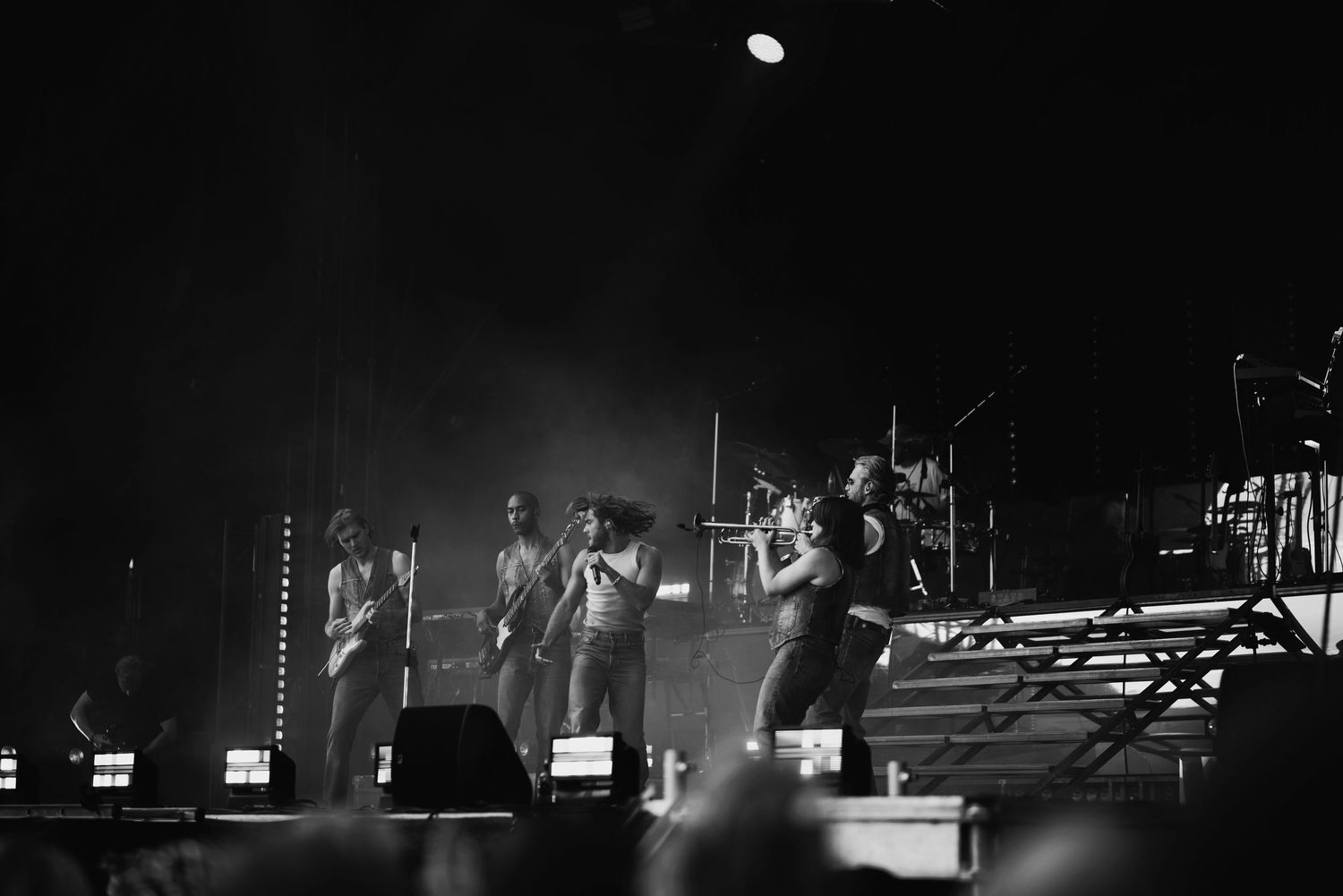Black and white concert photo of band performing on stage with dramatic lighting.