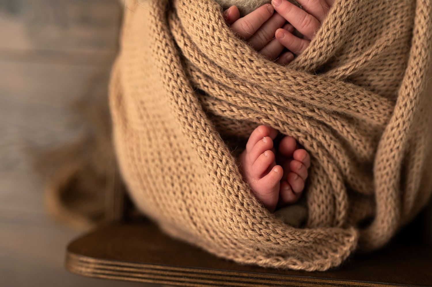 Close-up of tiny baby feet peeking through warm knitted beige blanket.