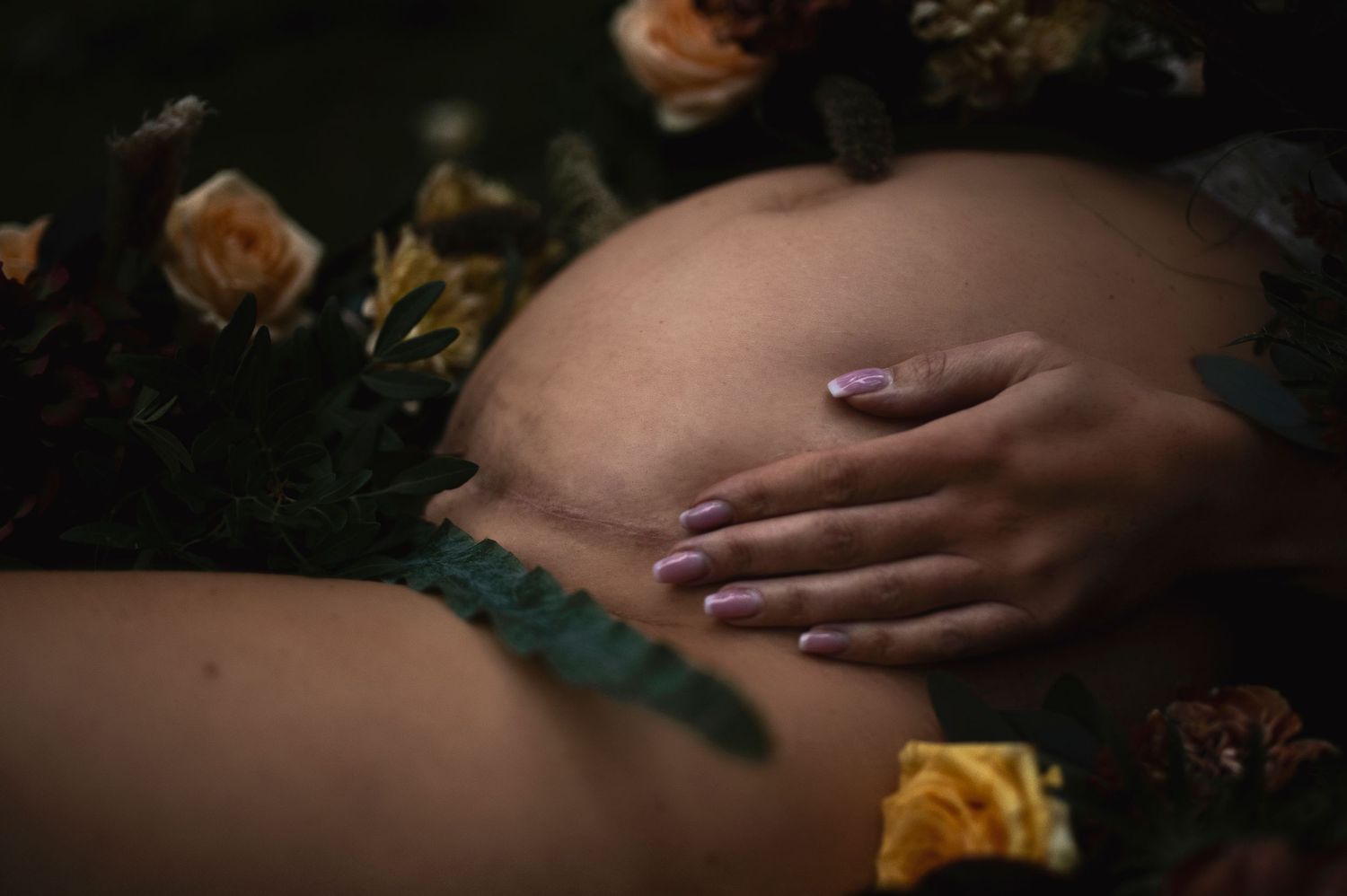 Close-up maternity photo with yellow roses and hands cradling belly.