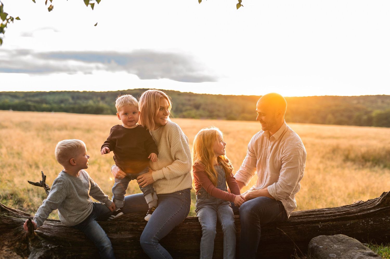 Family sharing intimate moments while relaxing on log in golden field.