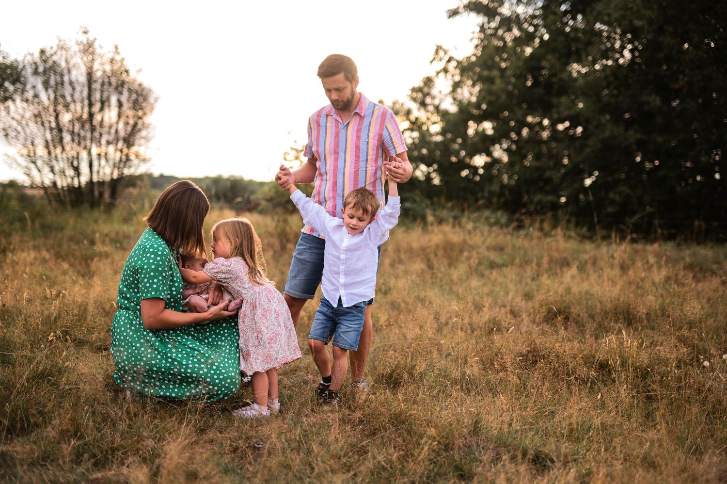 A tender family scene on a grassy hillside at golden hour wearing coordinated summer outfits.