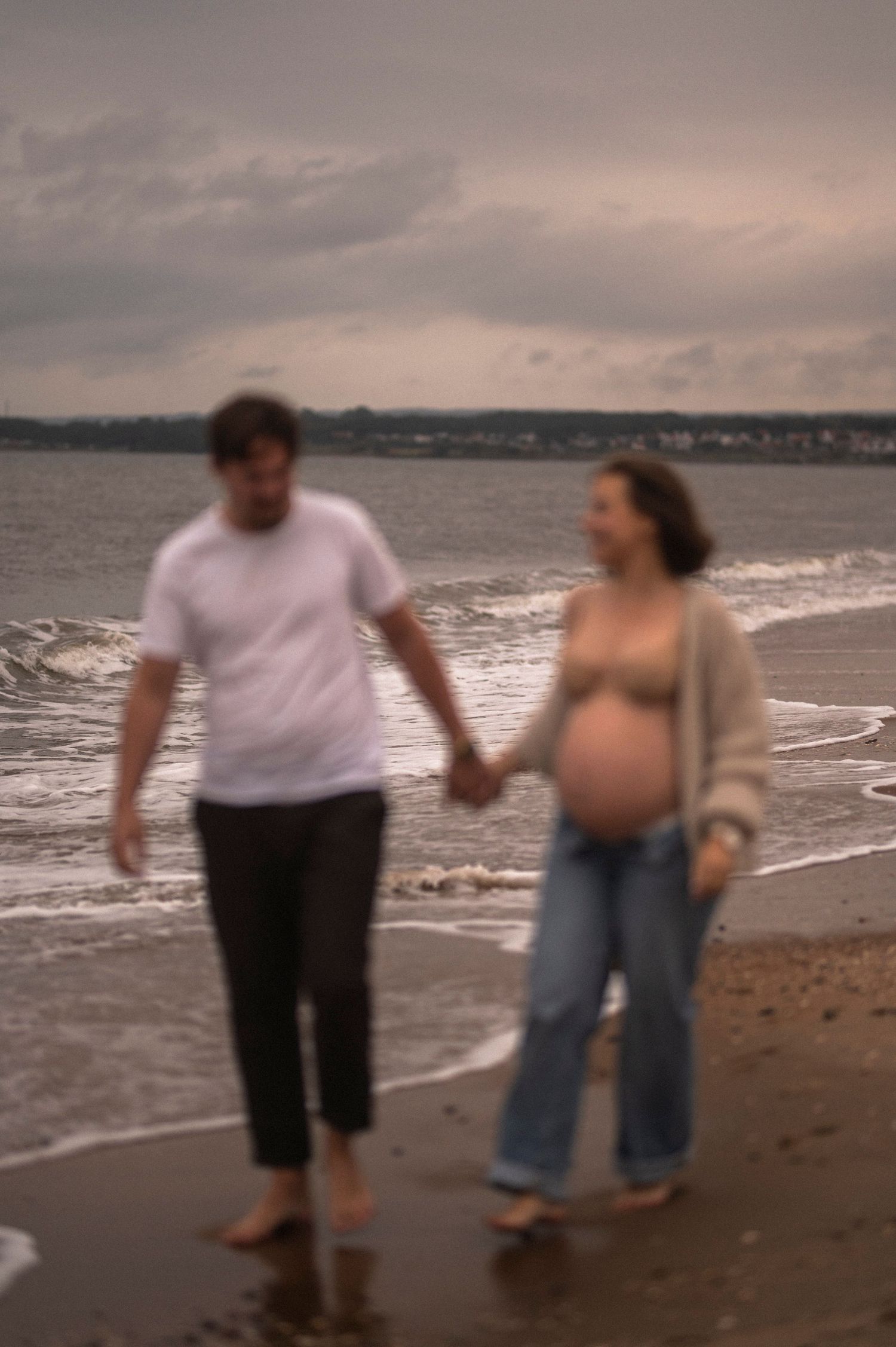 A couple holds hands while walking along the shoreline during sunset.