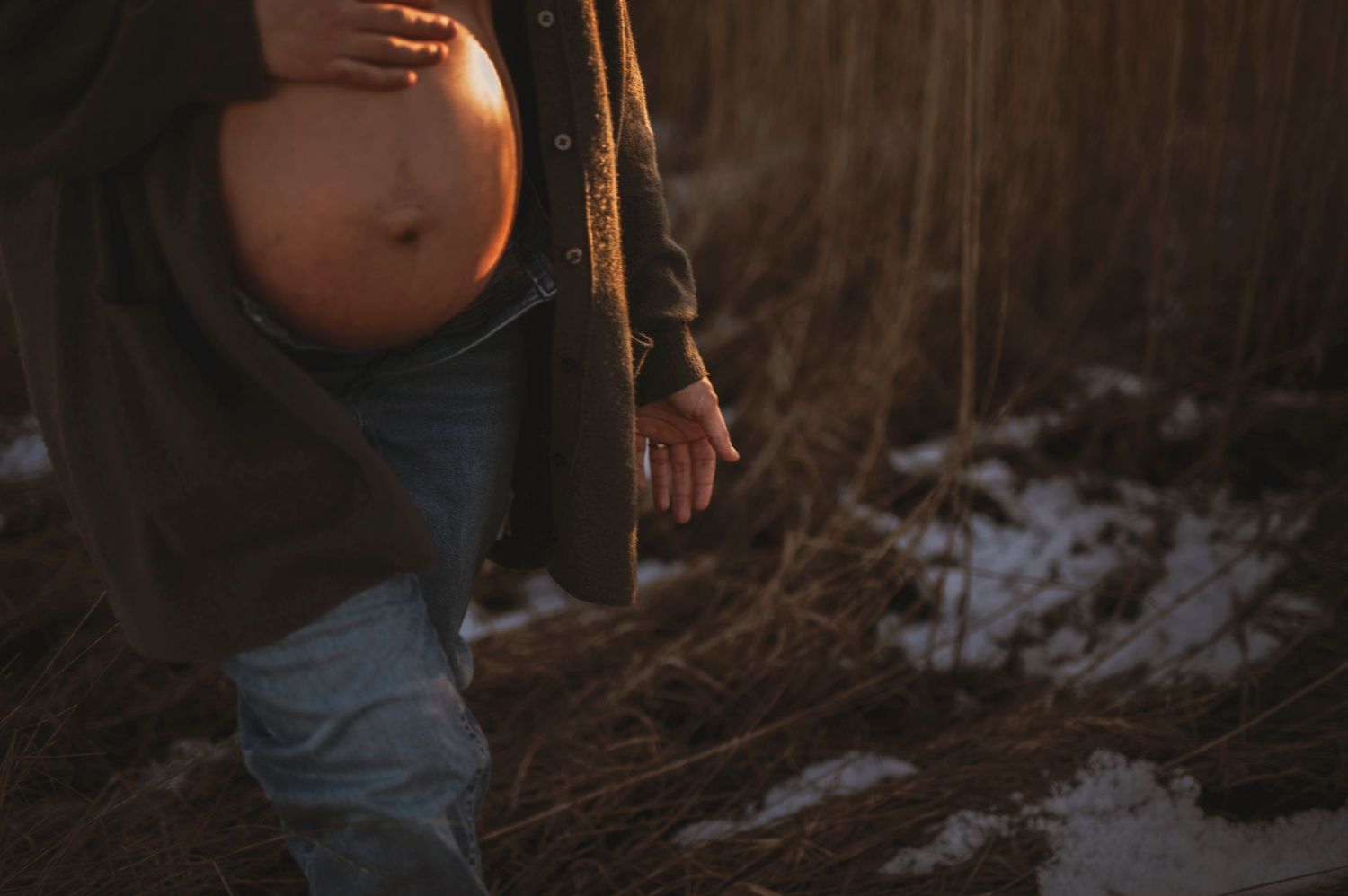 Close-up shot of pregnant belly in natural outdoor setting with snow and reeds.