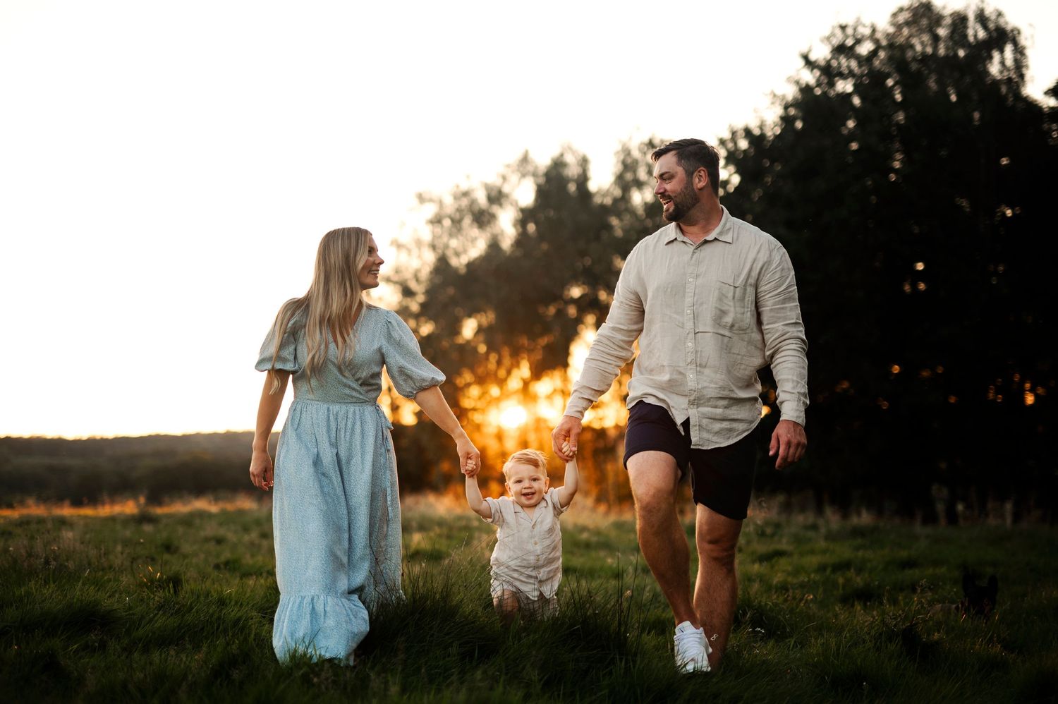 A family holds hands while walking through a grassy field at sunset.