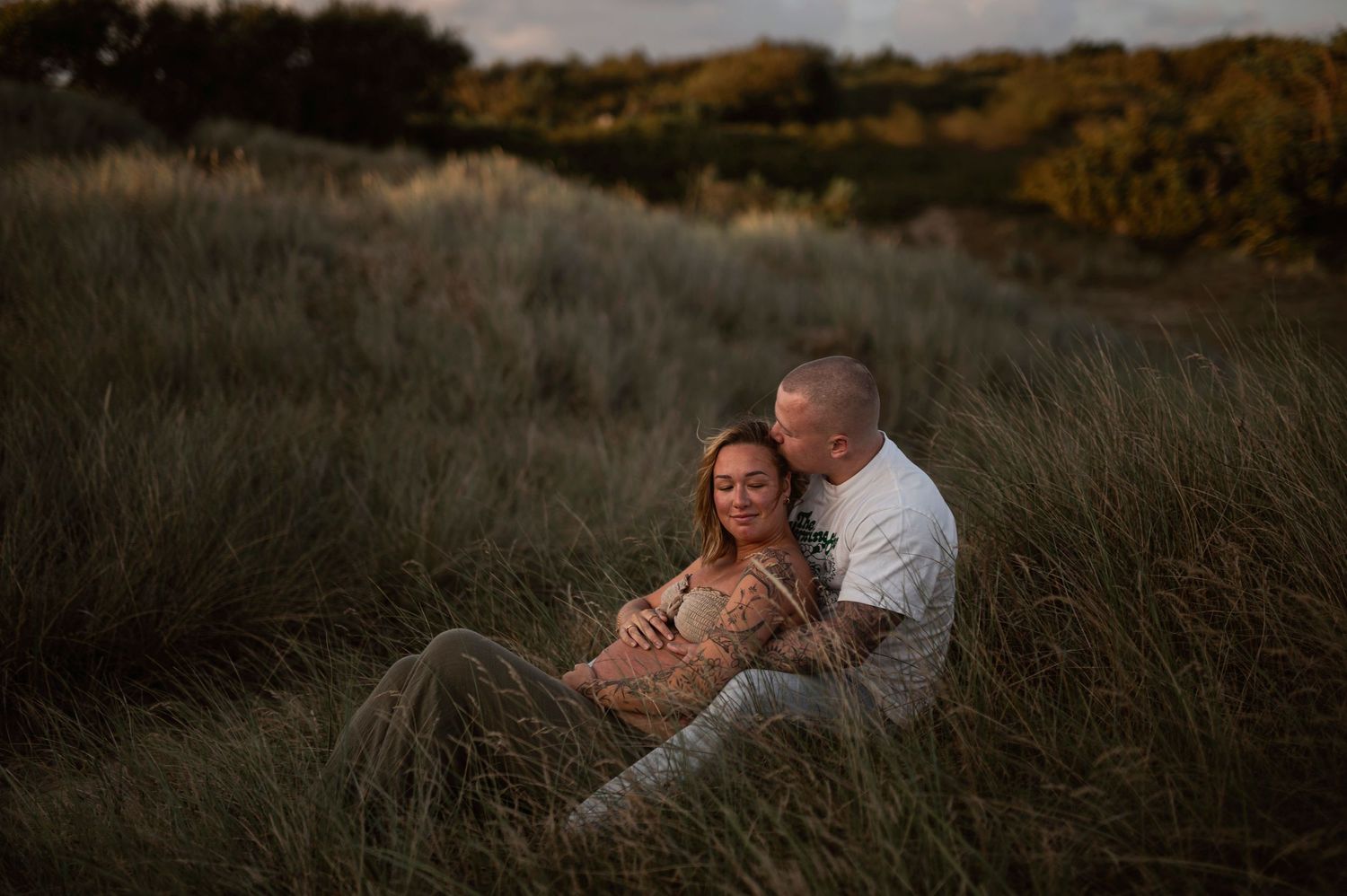 Couple embracing in tall grass during a golden sunset session.