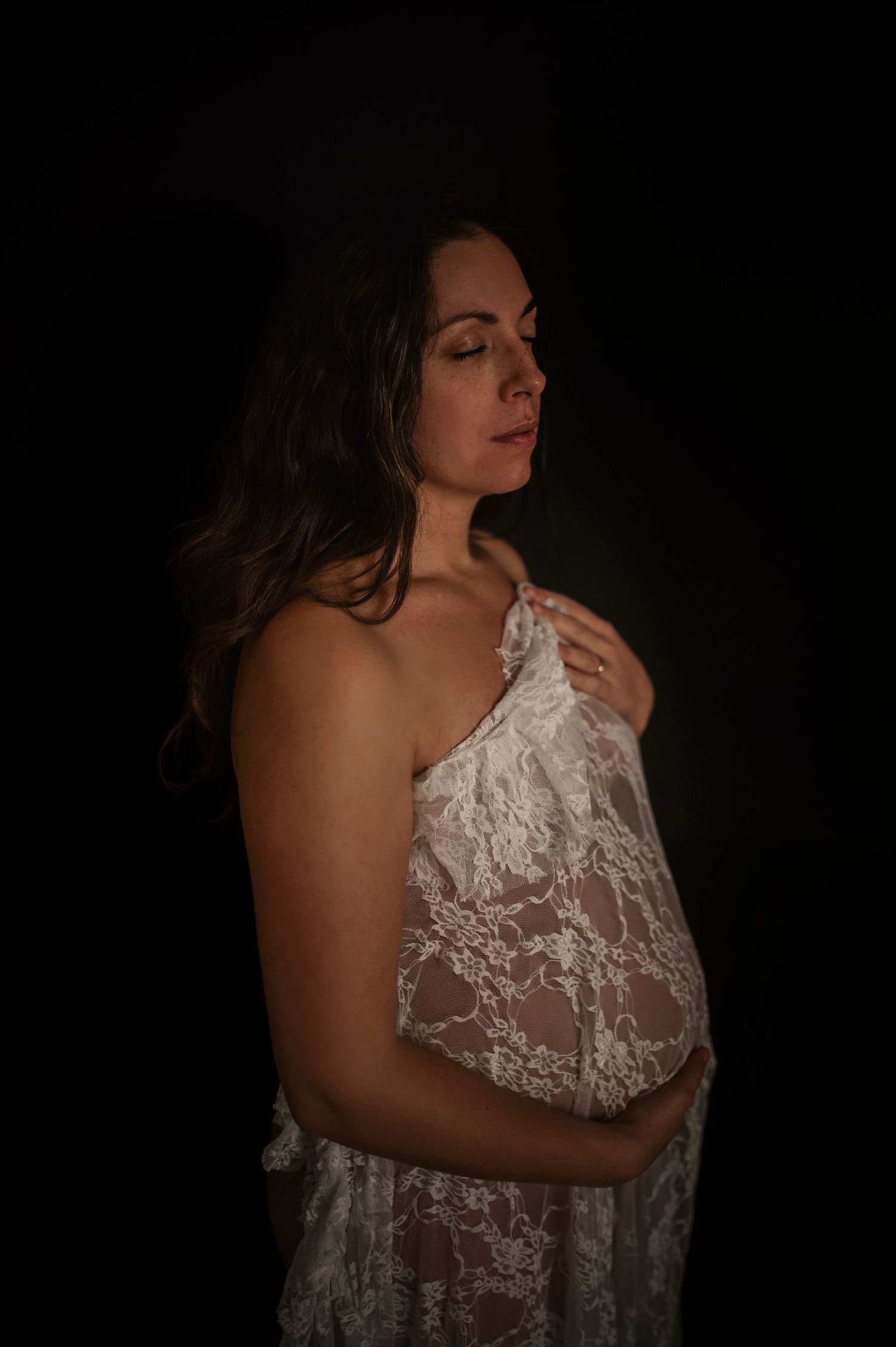Intimate maternity portrait with soft lighting and flowing white lace fabric.