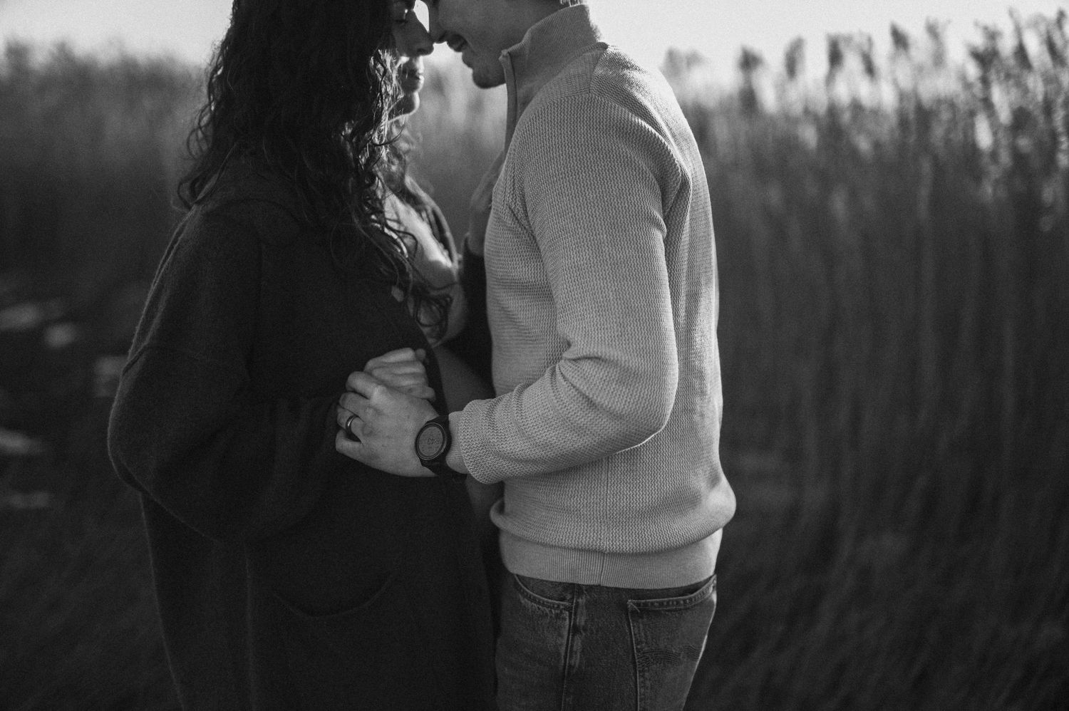 Intimate black and white maternity photo of couple embracing among tall grass.