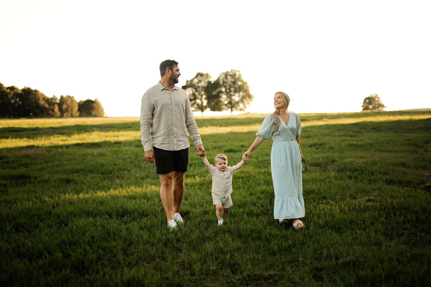 Family walking together holding hands in a grassy field during golden hour.