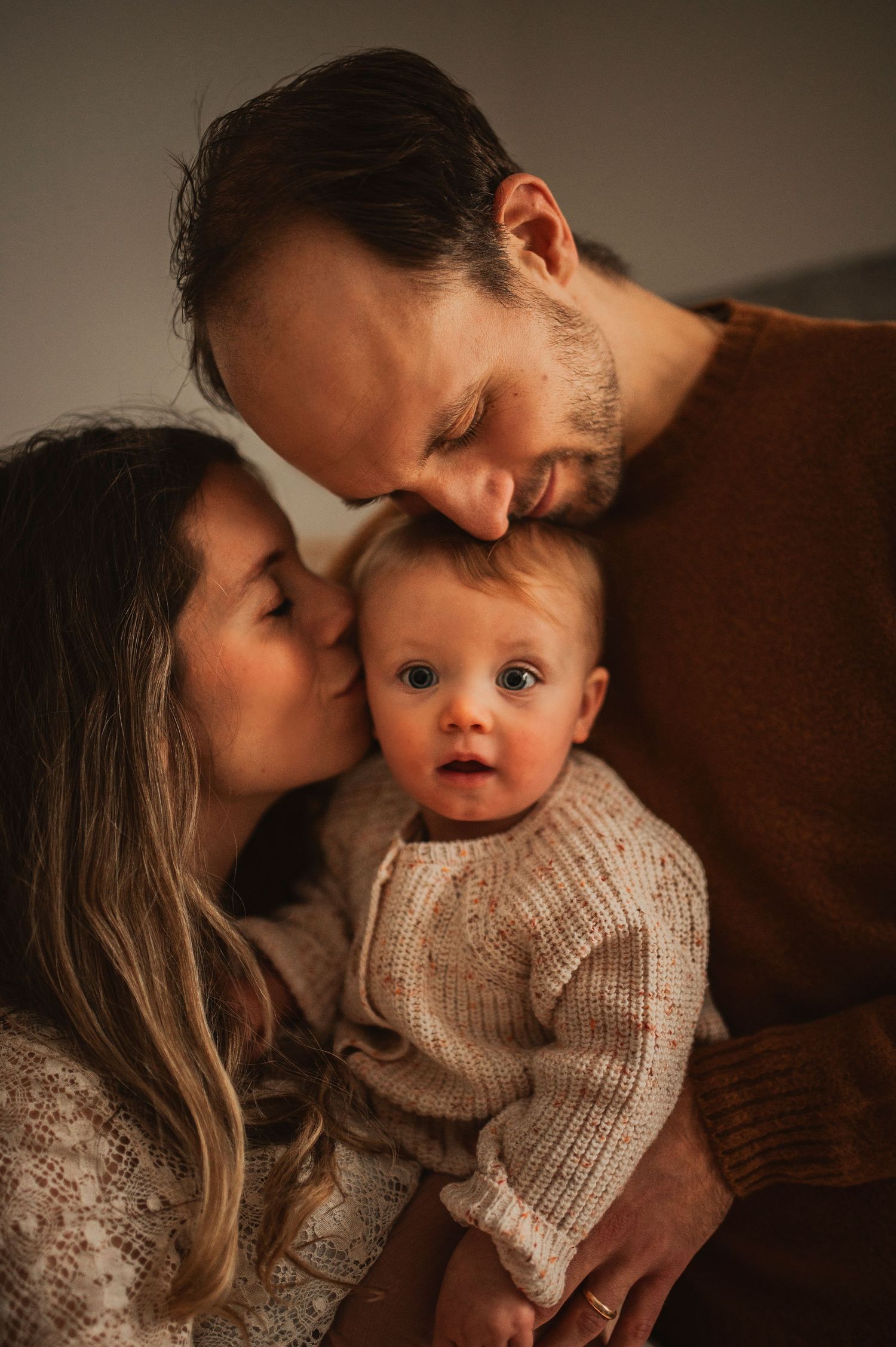 Tender family moment captured in warm lighting with knit sweaters and soft expressions.