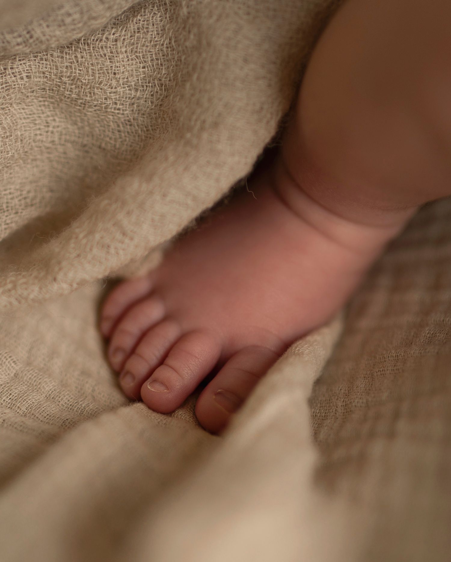 Close-up of baby's tiny foot peeking out from under beige blanket.