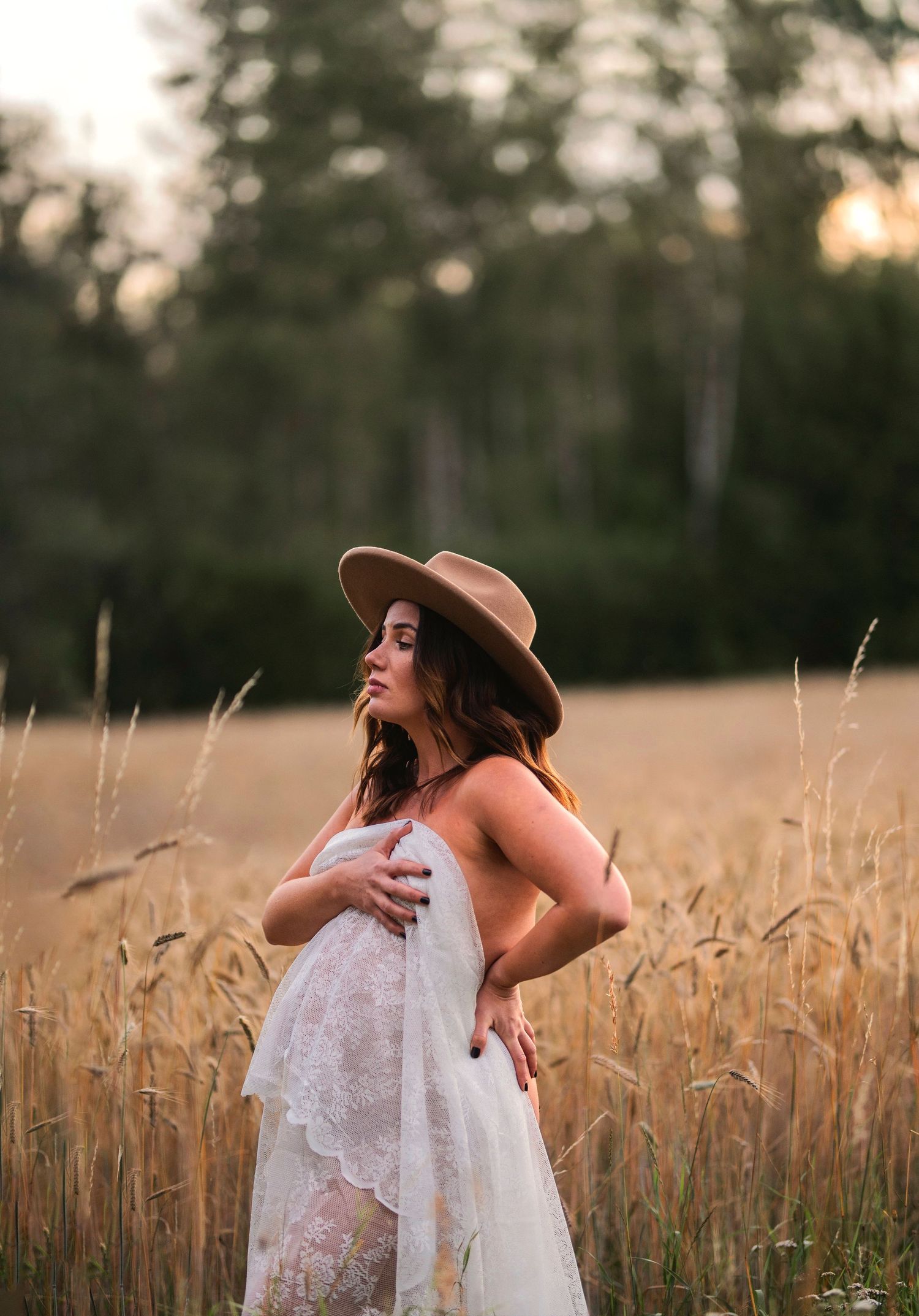 Maternity photo in wheat field with woman wearing boho dress and hat at golden hour.
