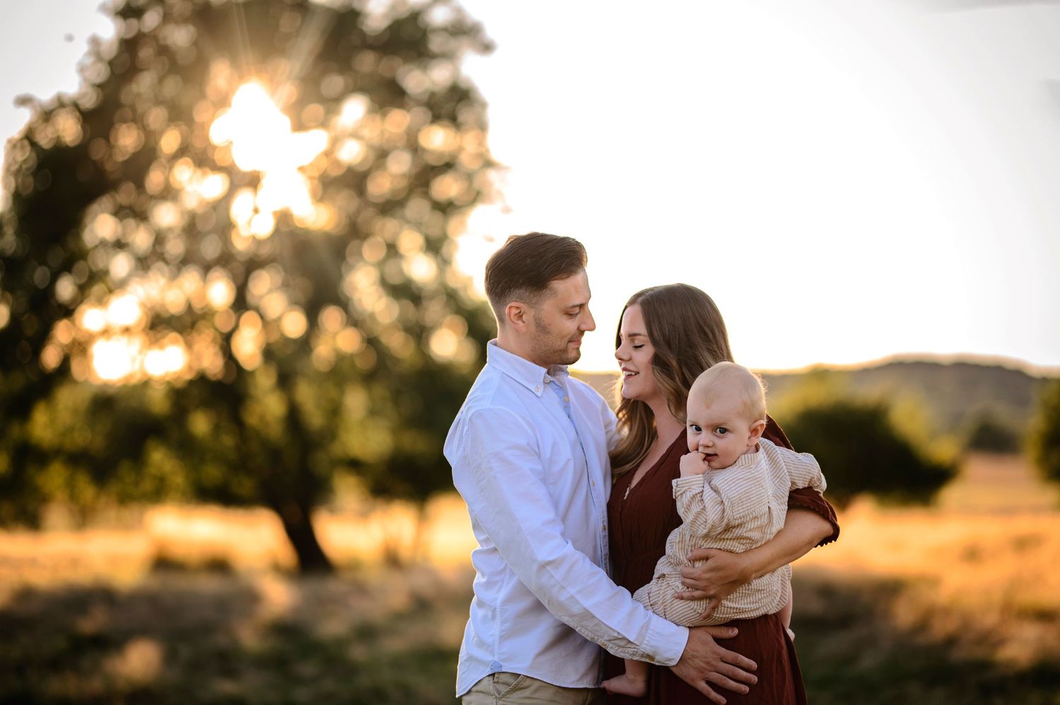 Family enjoying tender moment together in rustic field during golden hour sunset.