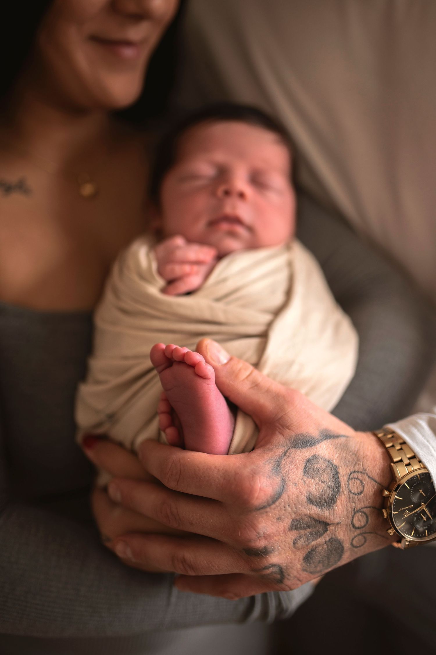 Close-up of tattooed hands holding newborn baby's tiny feet.