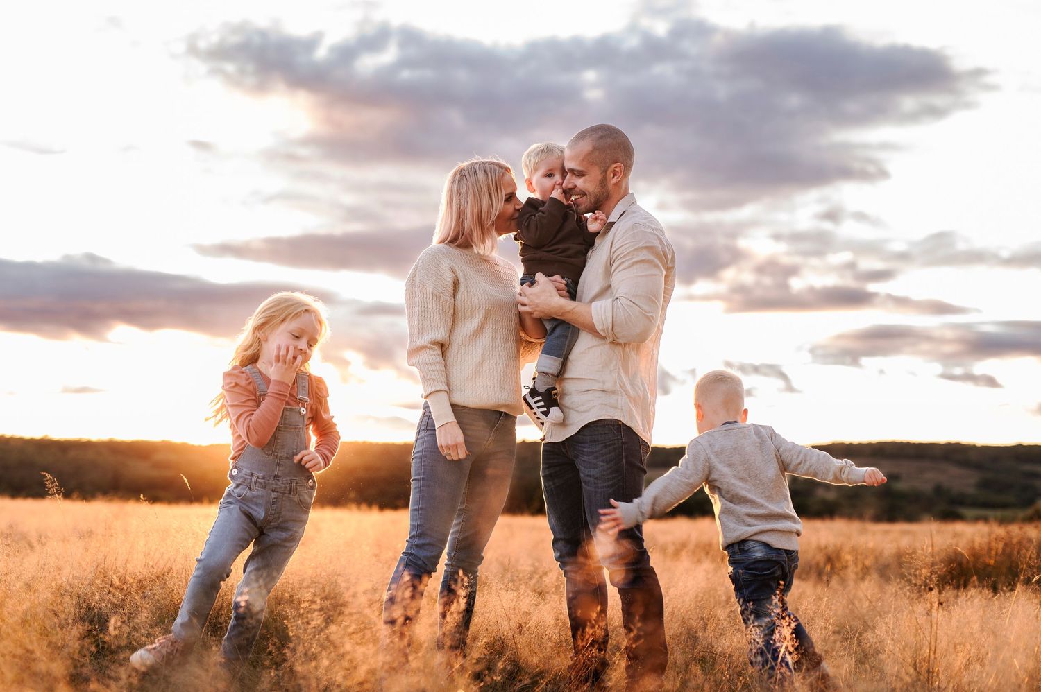 A loving family embraces in a sun-drenched field during golden hour at sunset.